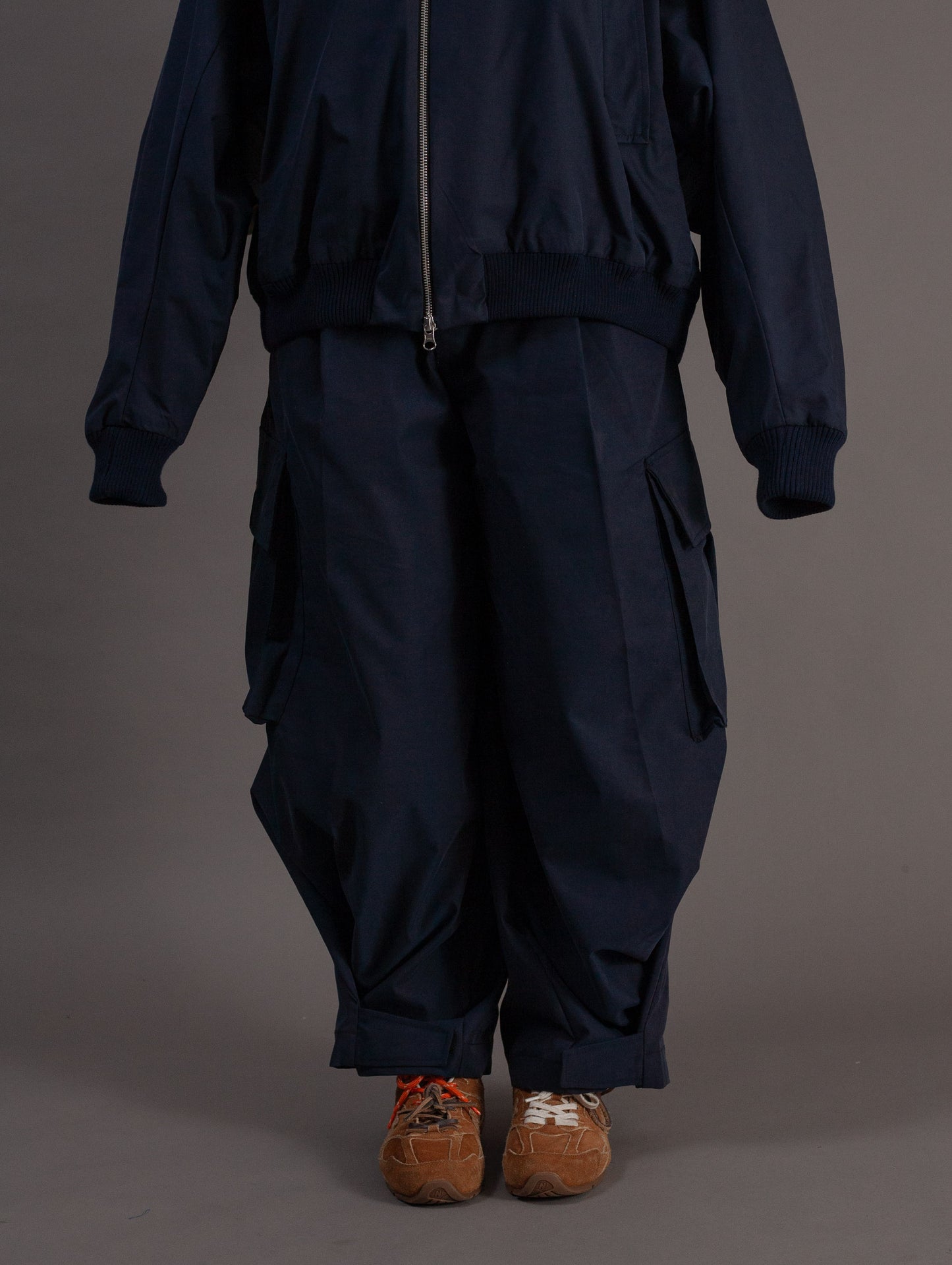 Person wearing a dark blue navy outfit with brown shoes on a gray background
