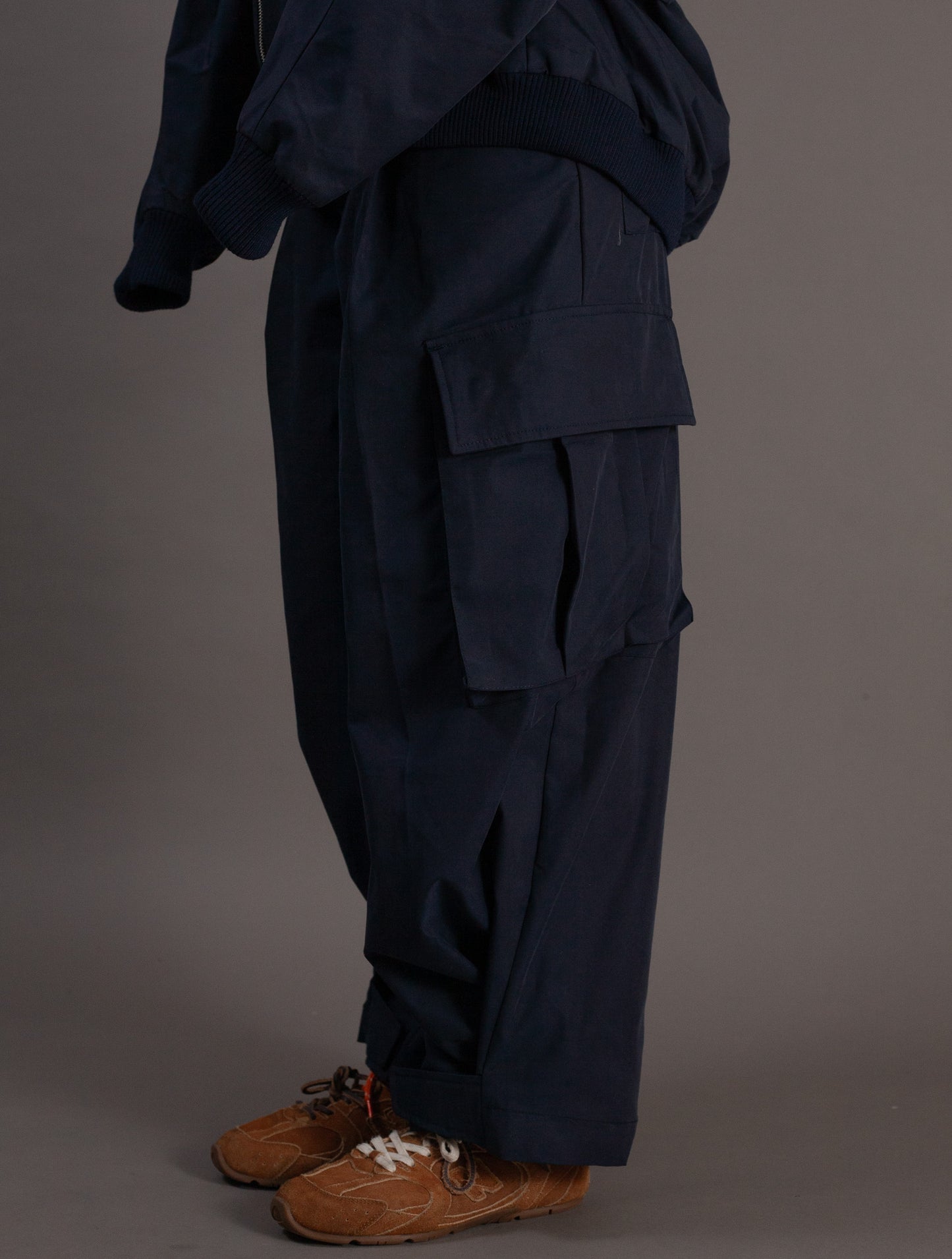 Person wearing navy cargo pants and brown shoes on a gray background
