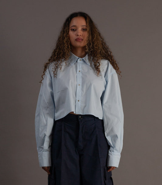 Person wearing a light blue shirt and dark pants on a gray background