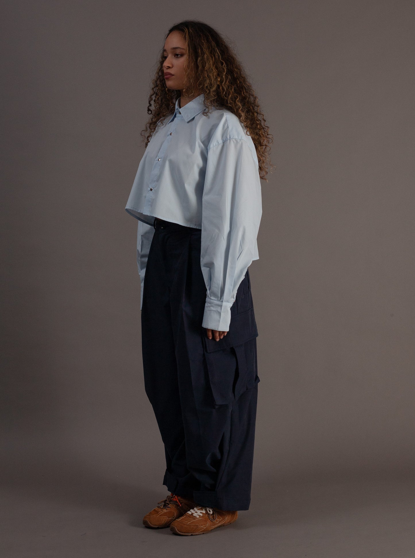 Person wearing a light blue shirt and dark pants against a gray background