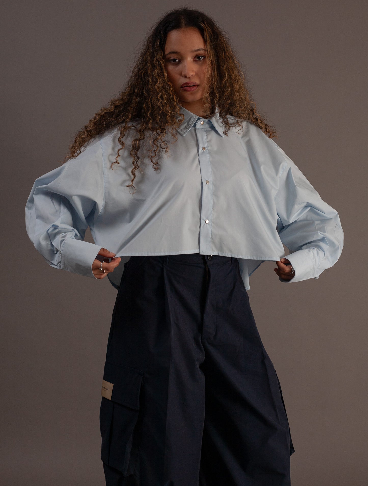 Woman wearing a light blue shirt and black pants against a gray background