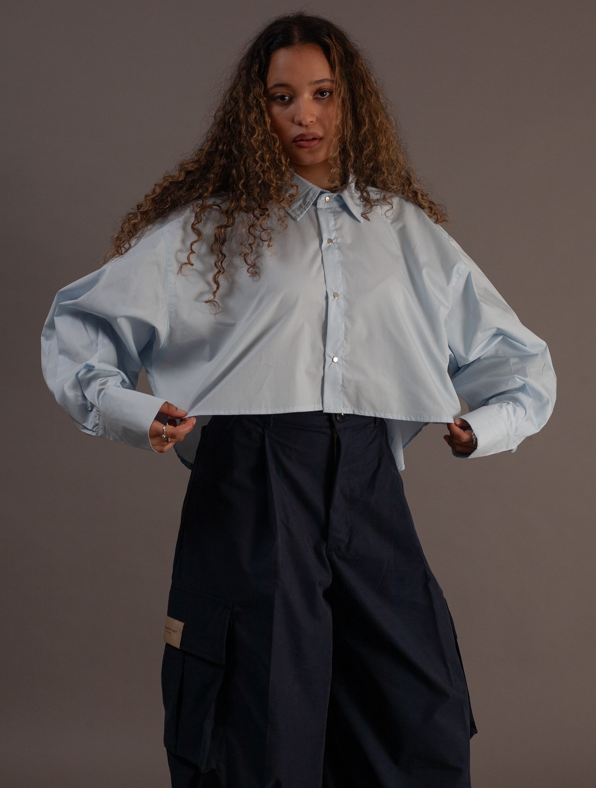 Woman wearing a light blue shirt and black pants against a gray background
