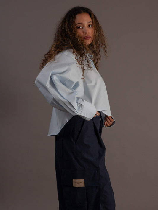 Woman wearing a light blue shirt and dark pants against a brown background