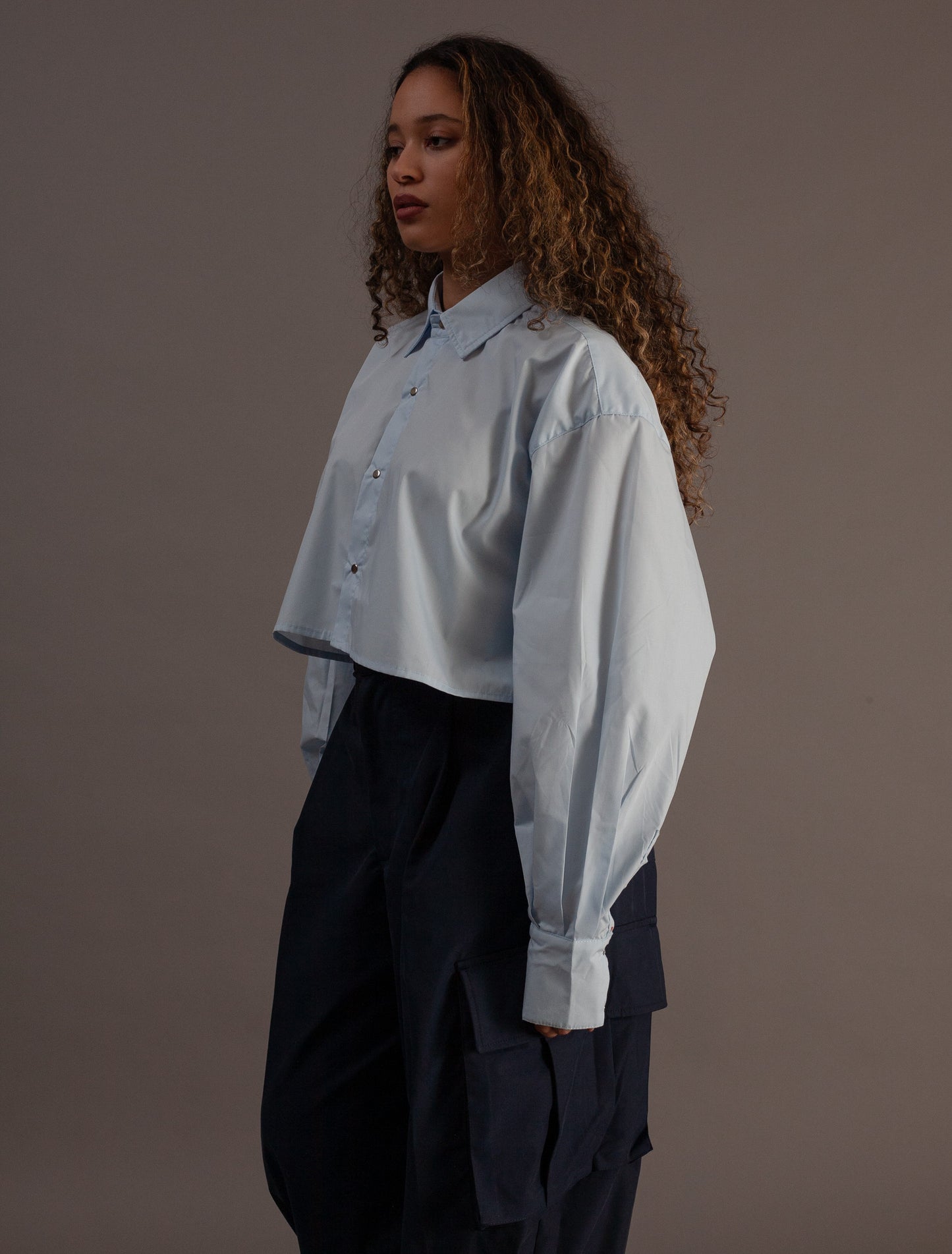 Person wearing a light blue shirt and dark pants against a plain background