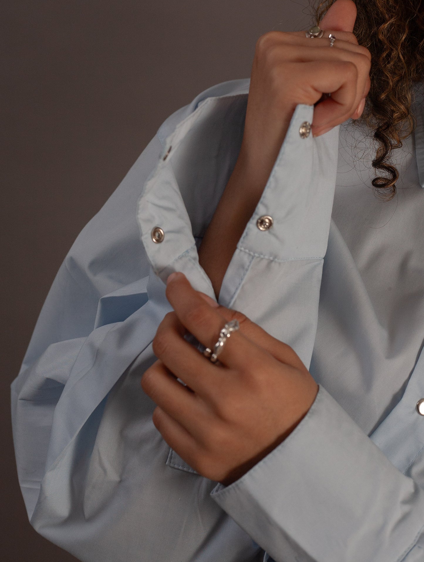 Person wearing a light blue jacket with gold buttons against a dark background