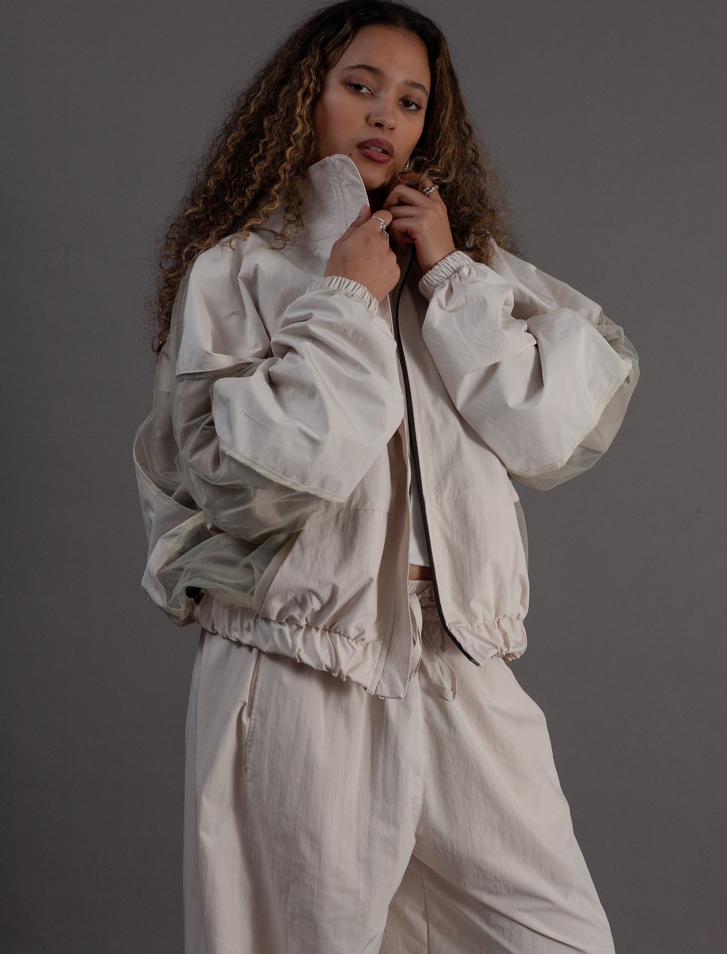 Woman wearing a light-colored outfit against a gray background