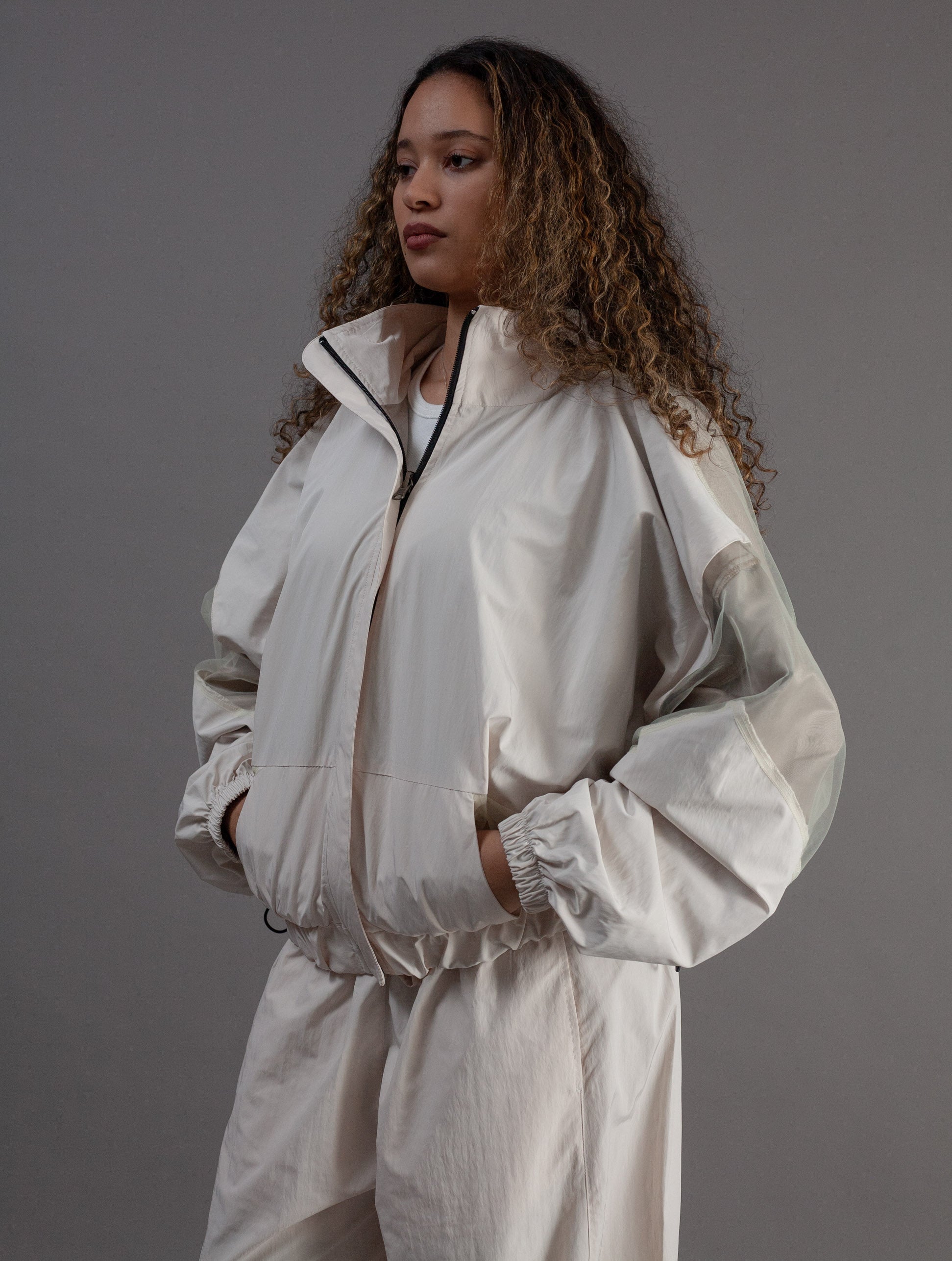 Woman wearing a light gray tracksuit against a gray background