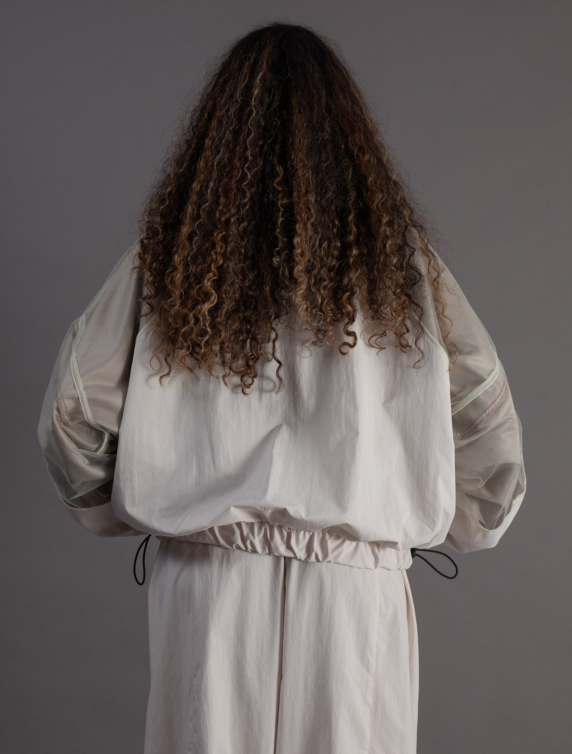Person wearing a light-colored outfit with long sleeves and a drawstring waist on a gray background