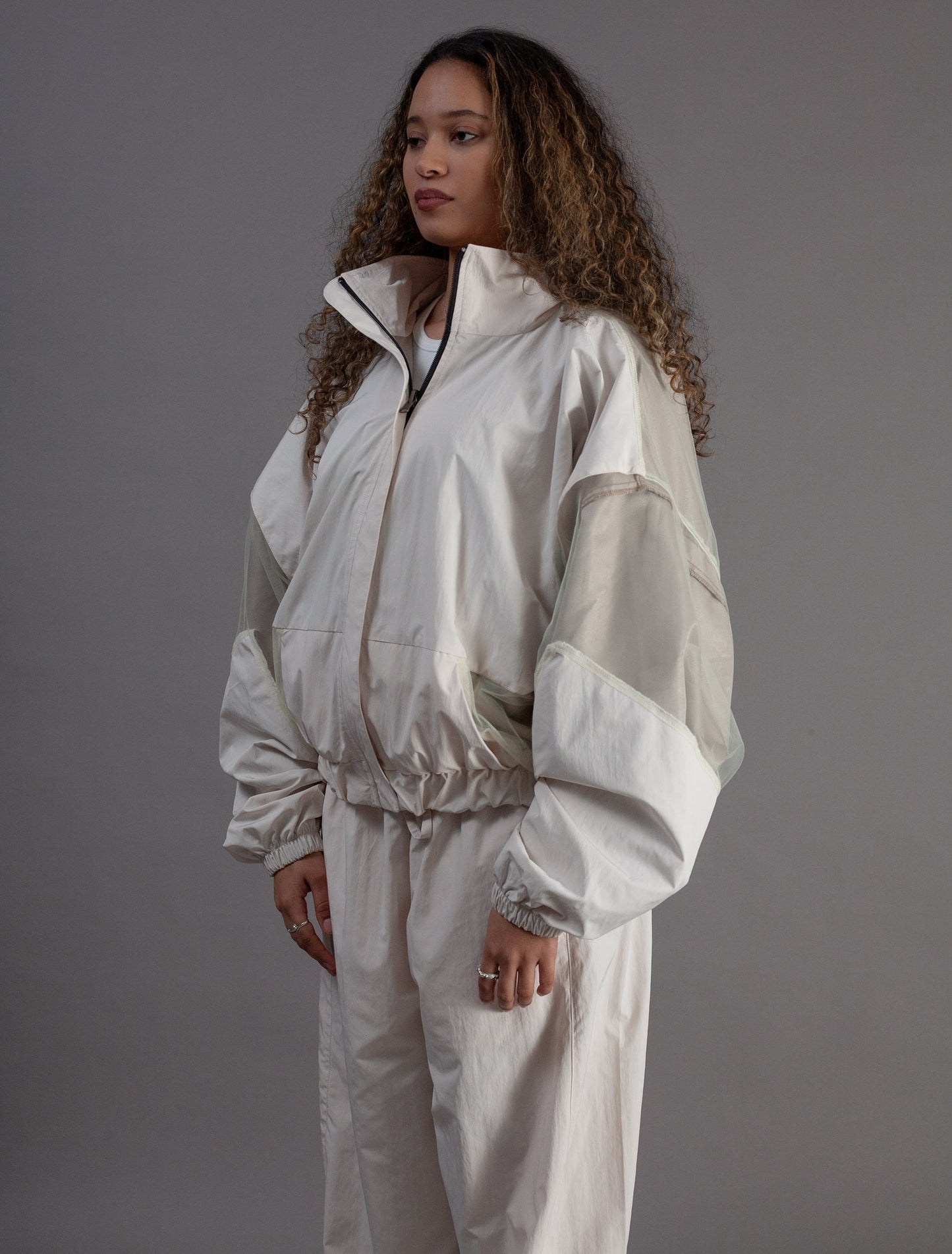 Person wearing a white tracksuit against a gray background