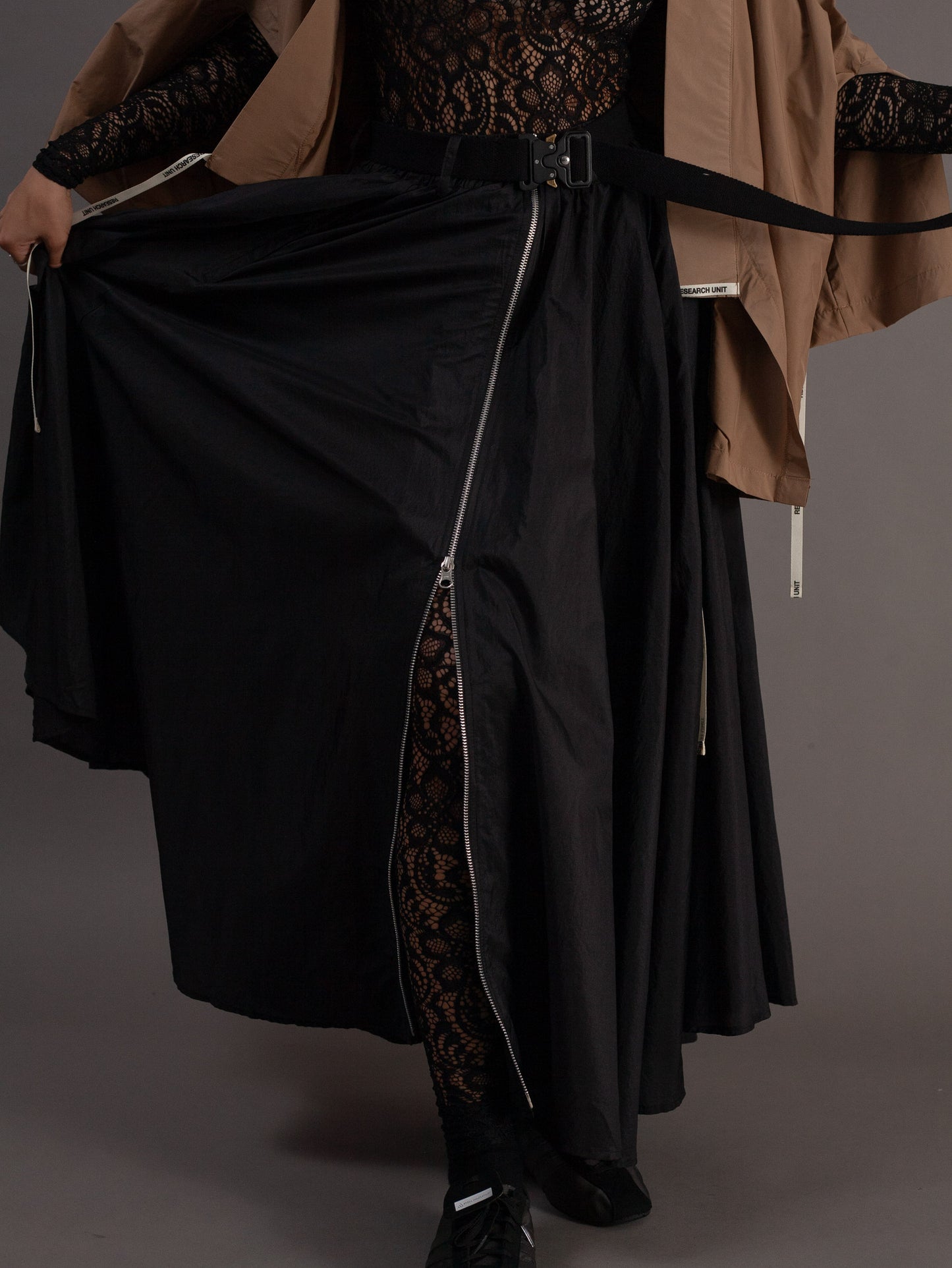 Person wearing a black outfit with a long skirt on a gray background