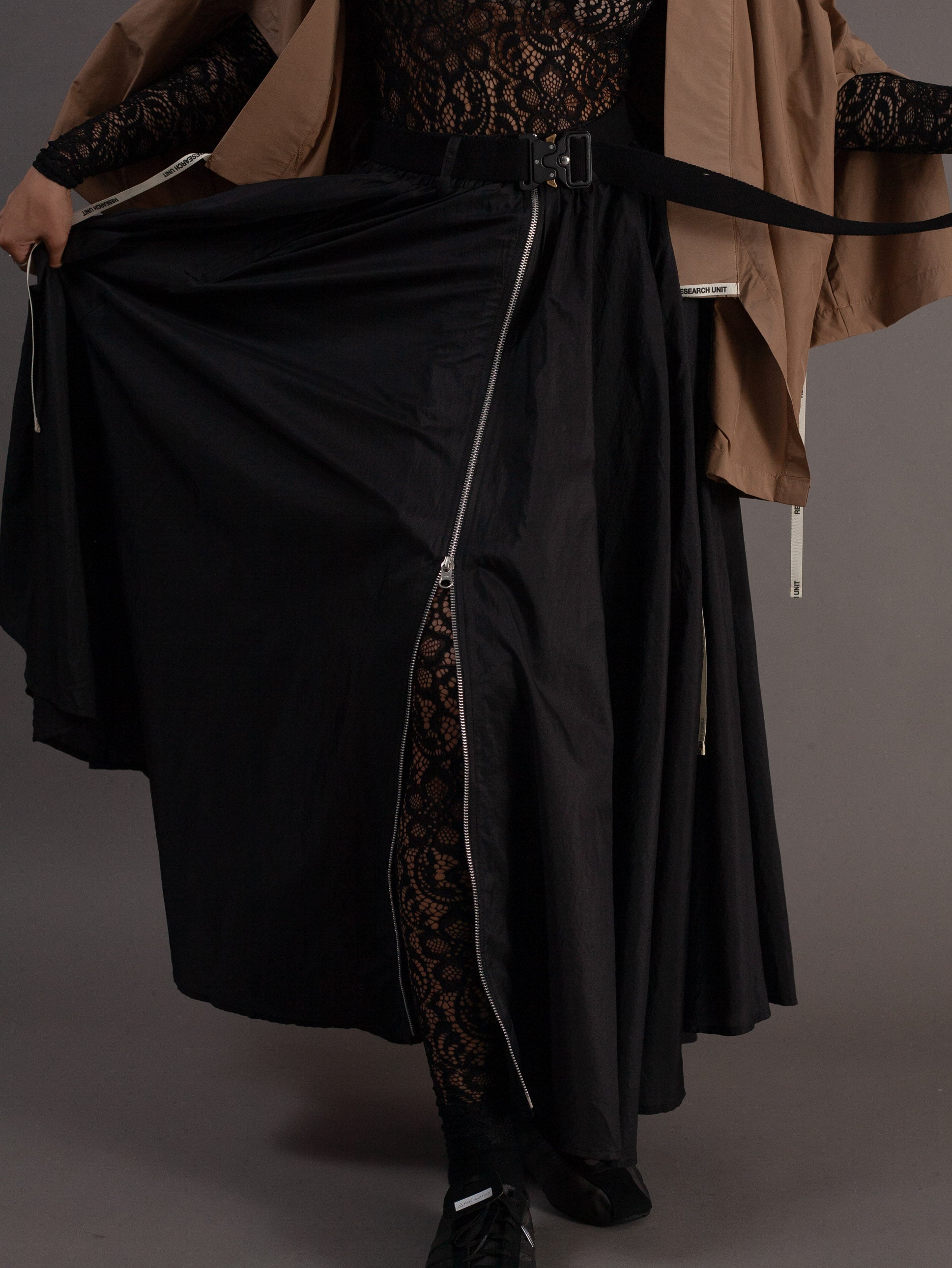 Person wearing a black outfit with a long skirt on a gray background
