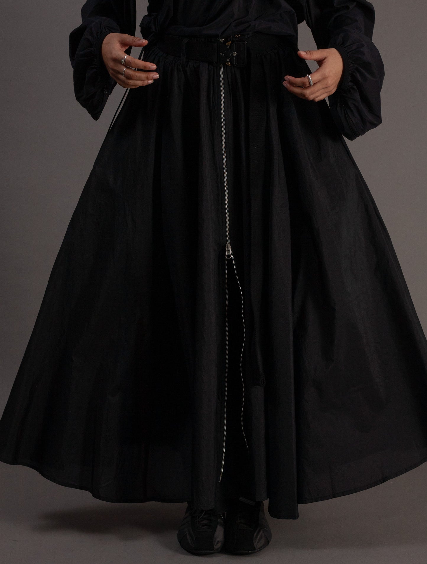 Person wearing a long black skirt with a plain background