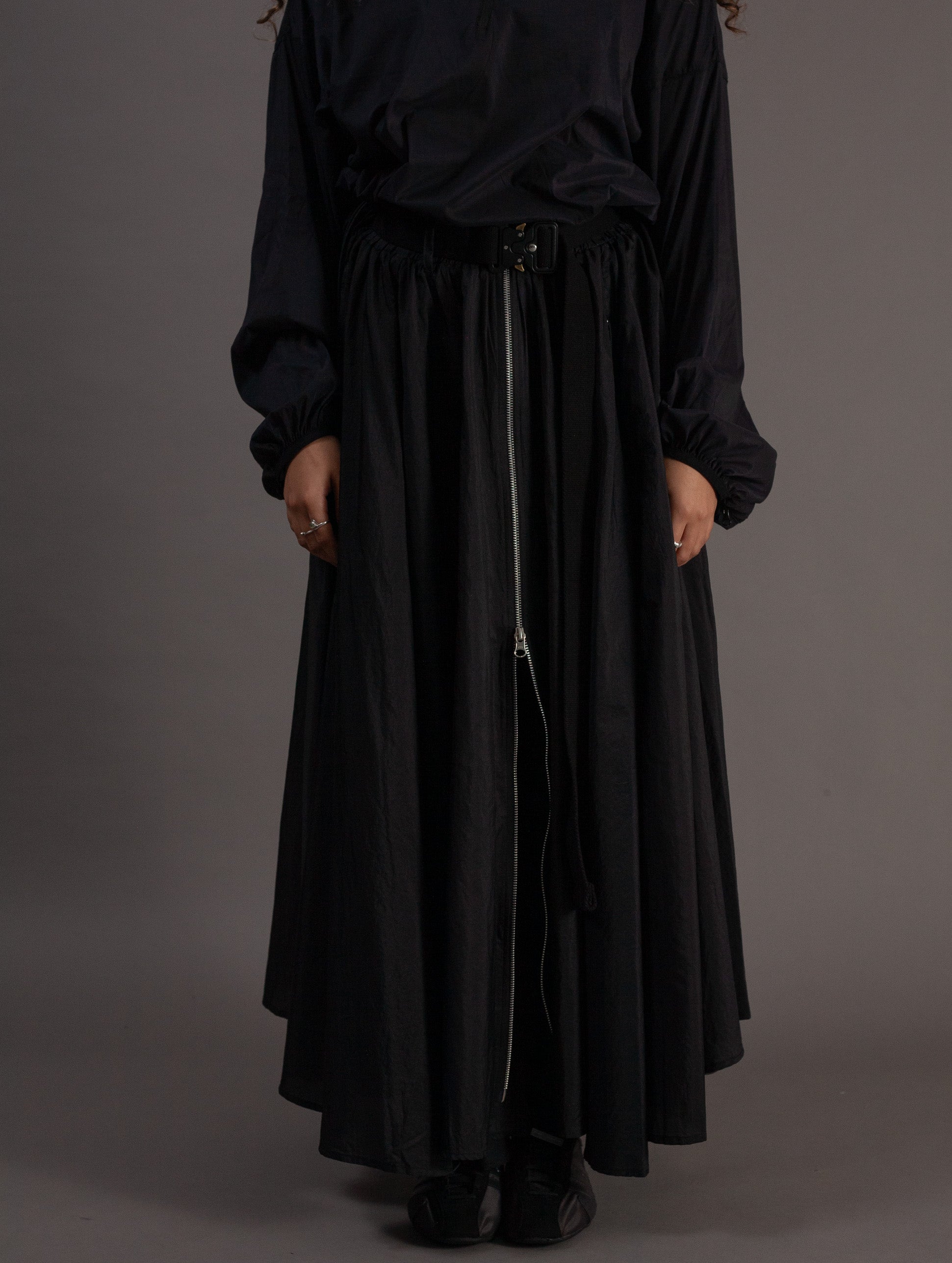 Person wearing a black outfit with a long skirt on a gray background