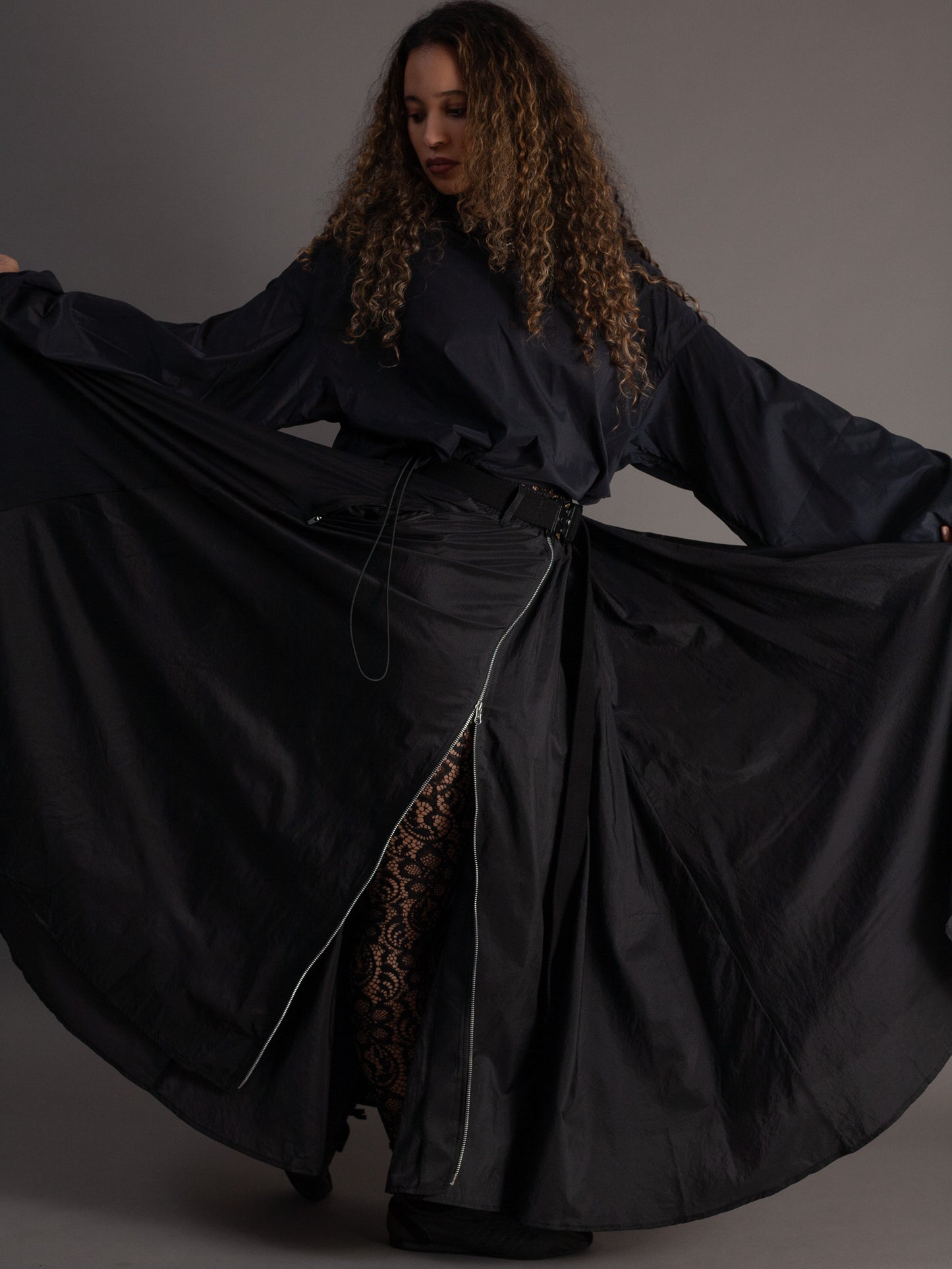 Woman wearing a long black garment with a slit on a gray background