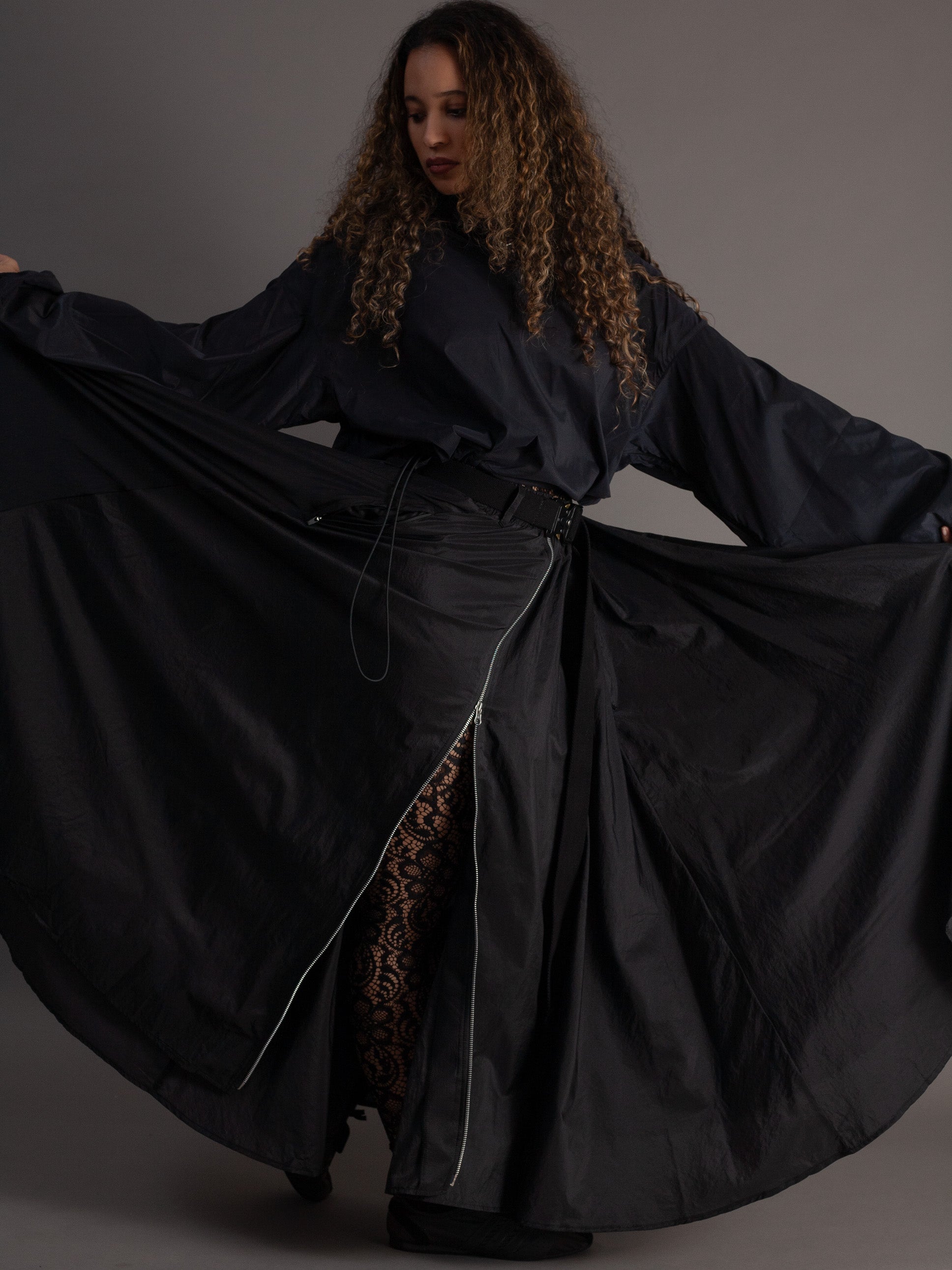 Woman wearing a long black garment with a slit on a gray background