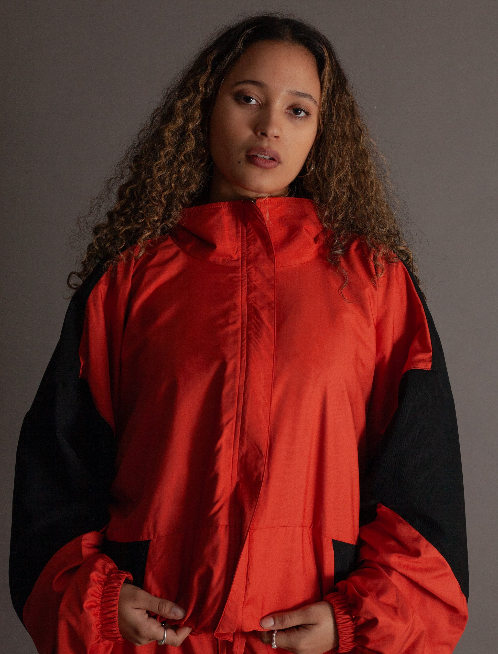Person wearing a orange and black jacket against a gray background