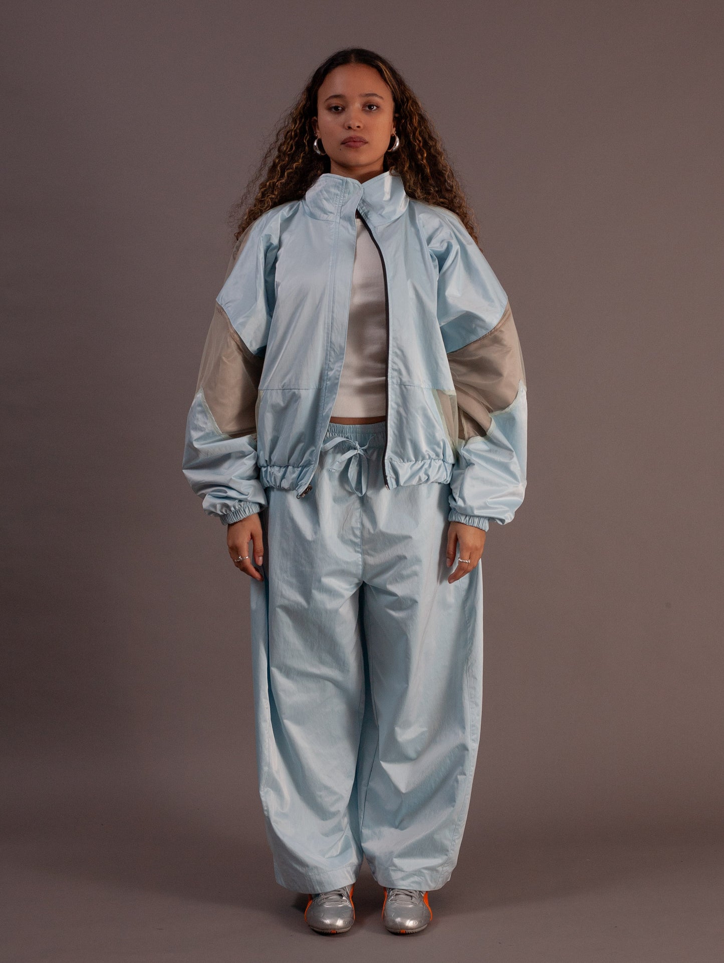 Person wearing a light blue and beige top and barrel pants against a brown background