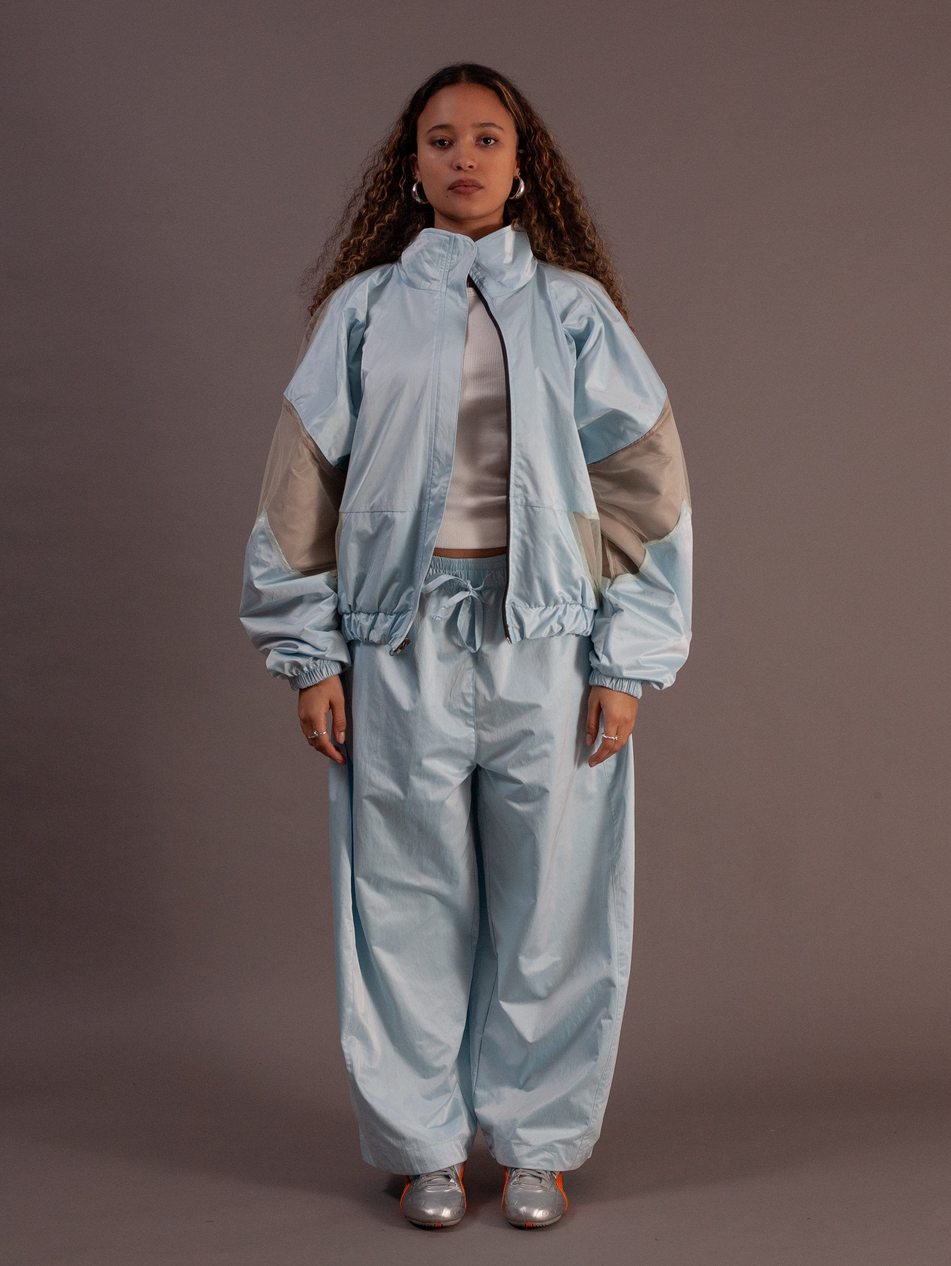 Person wearing a light blue and beige top and barrel pants against a brown background