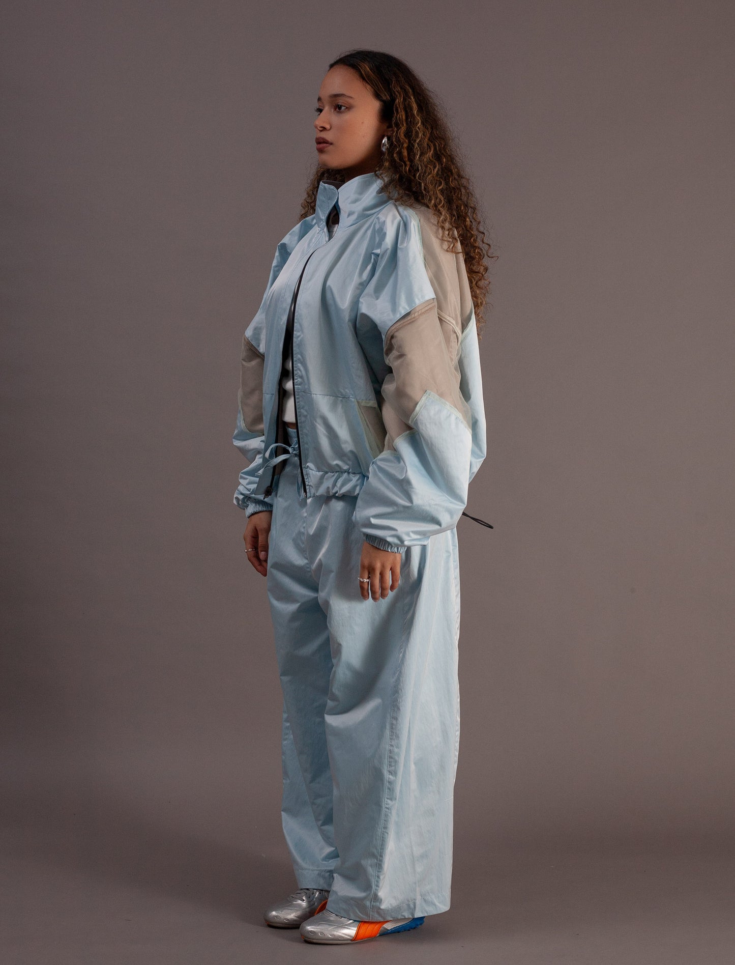 Person wearing a light blue and beige tracksuit against a gray background