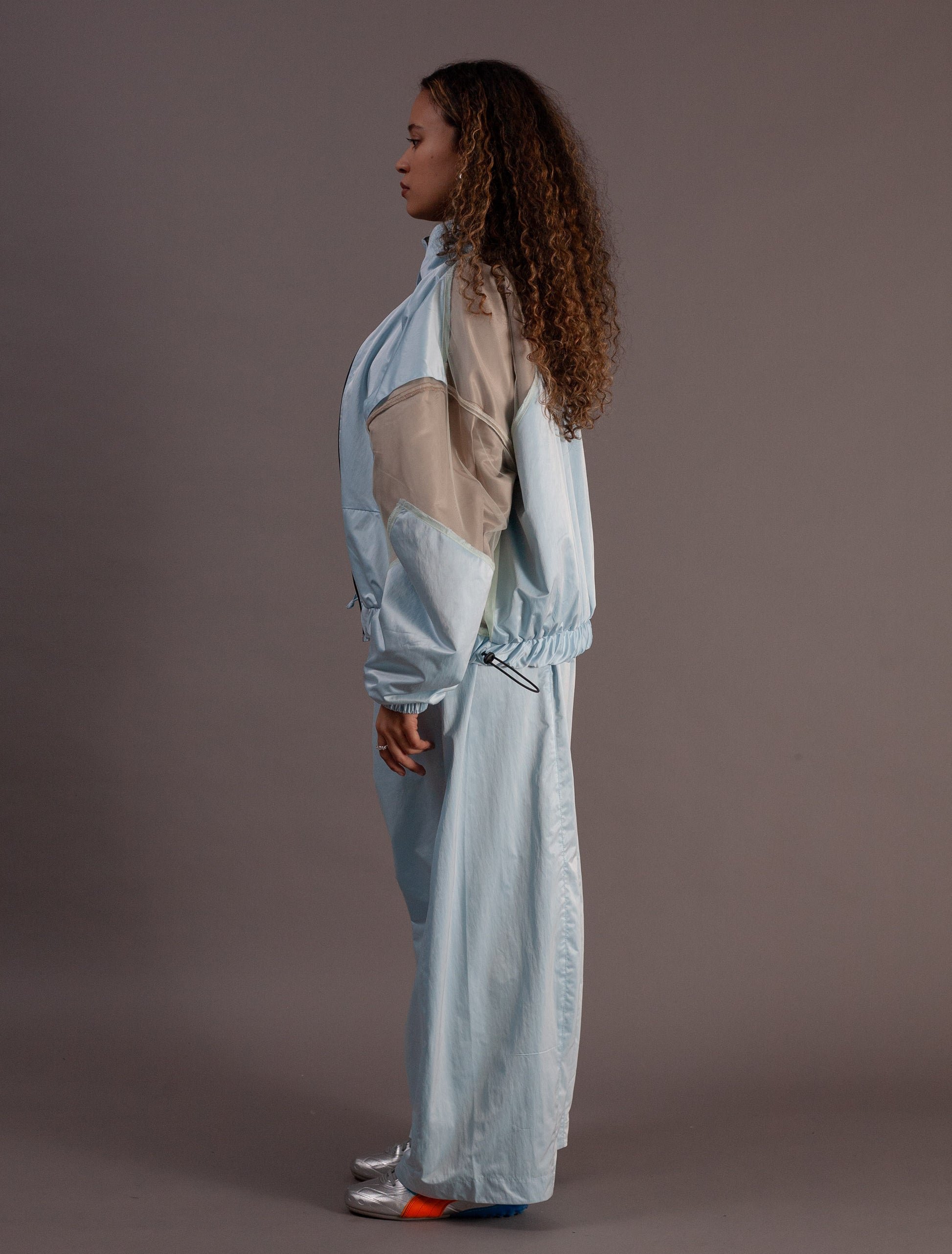 Person wearing a light blue tracksuit with beige accents on a plain background