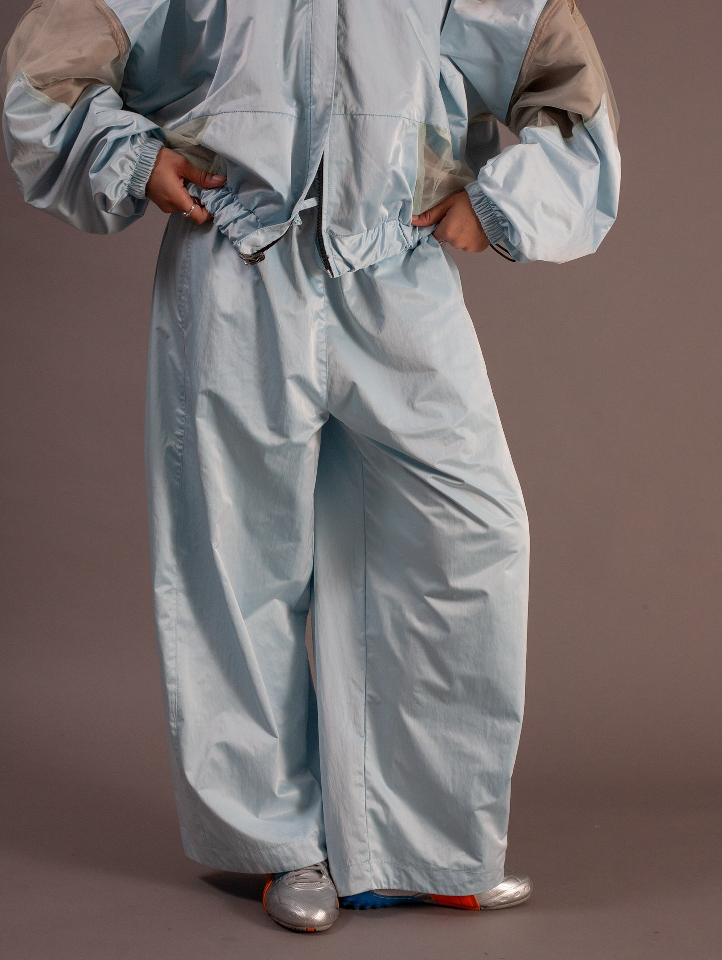 Person wearing a light blue sports jacket and pants on a brown background