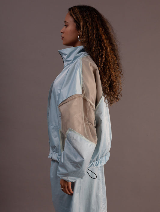 Person wearing a light blue and beige top and barrel pants against a brown background