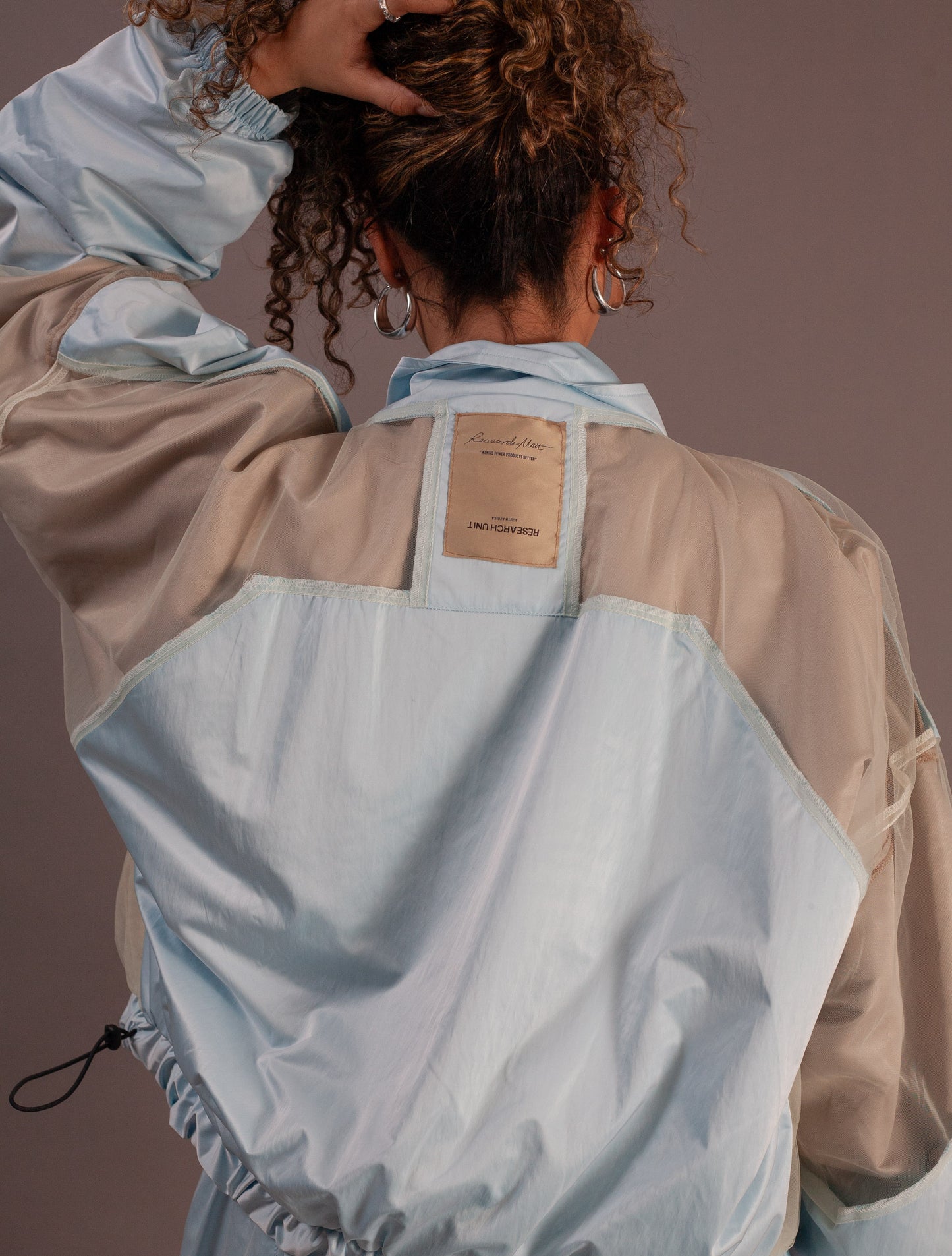 Person wearing a light blue and beige top and barrel pants against a brown background