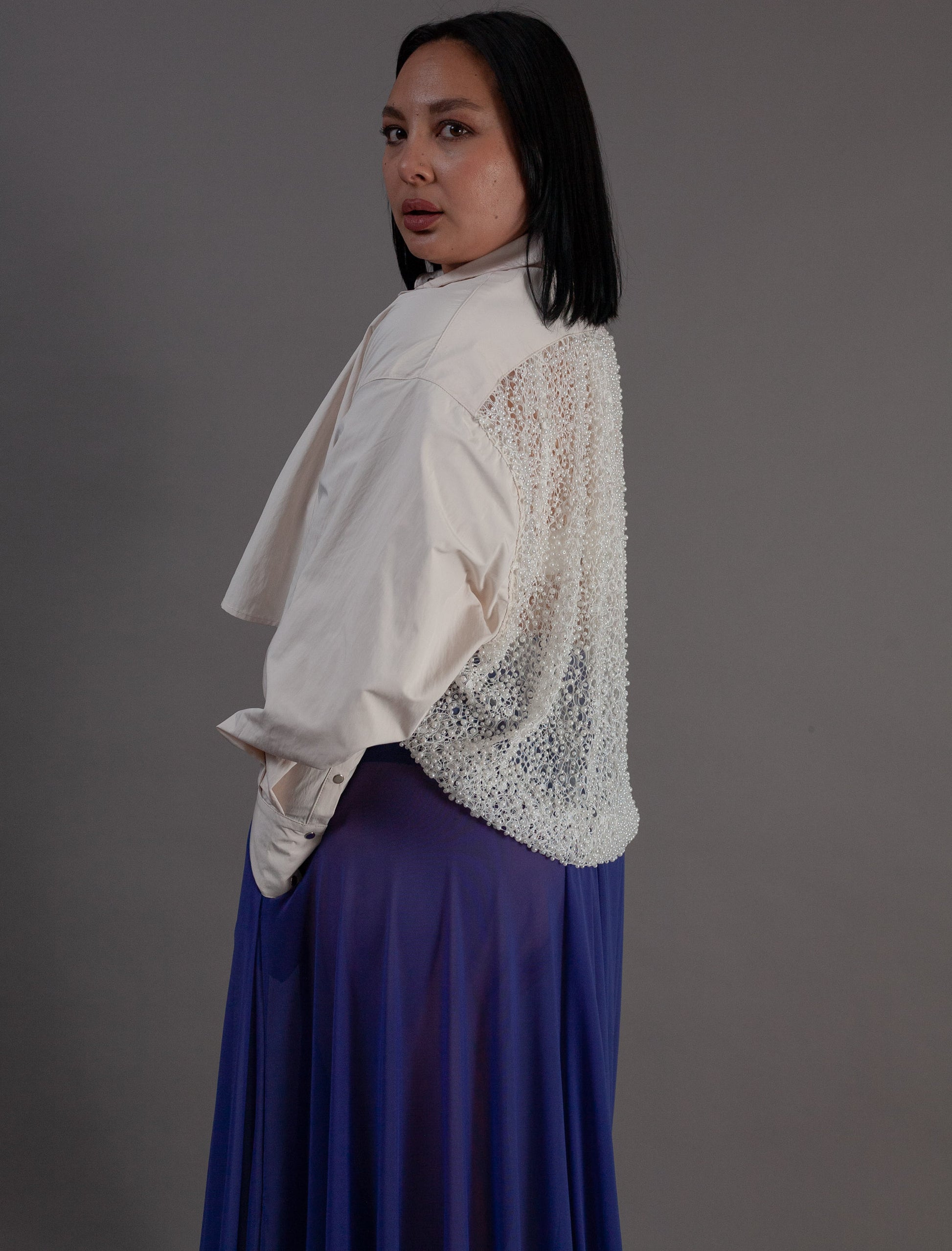 Woman wearing a white blouse with lace details and a purple skirt against a gray background