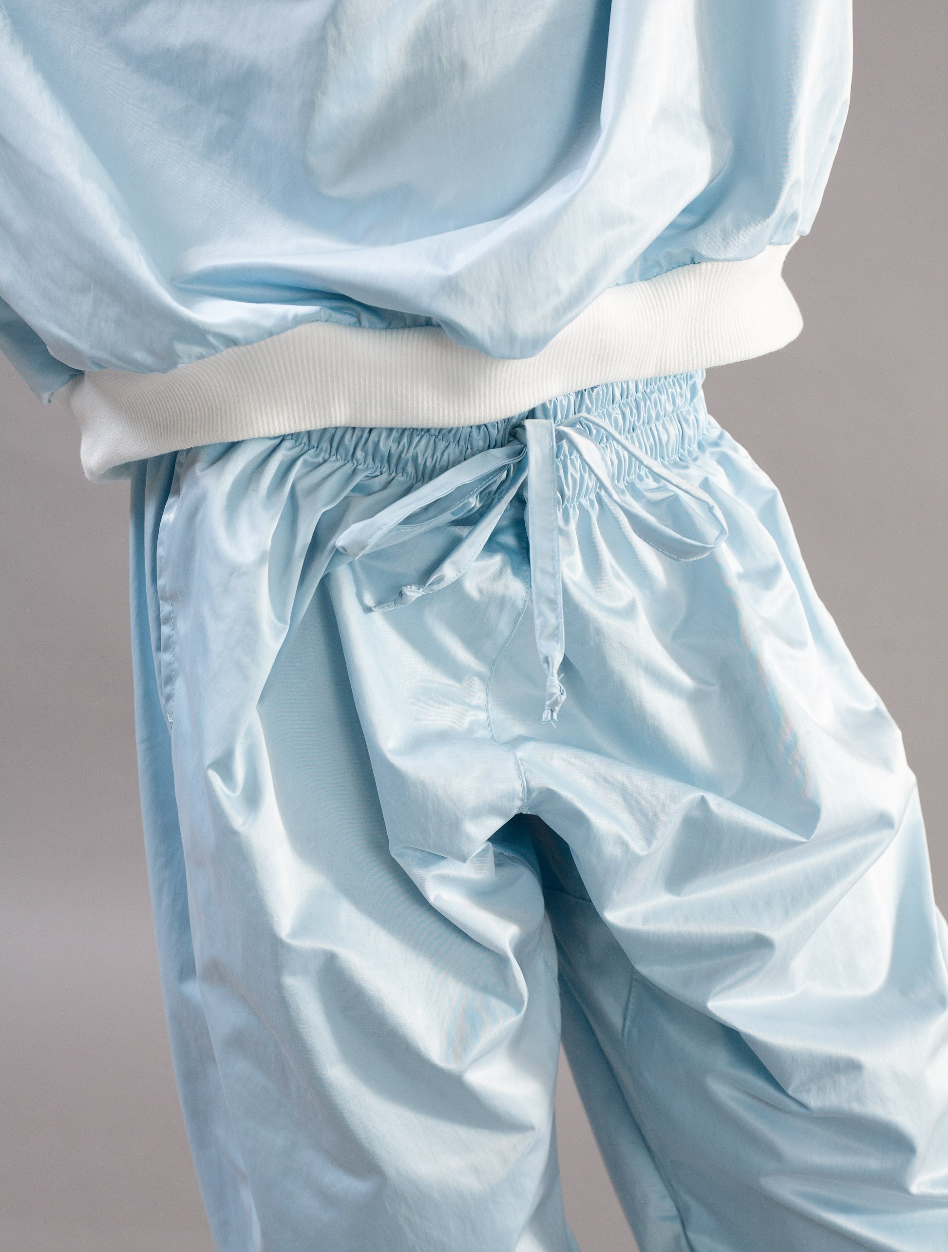 Close-up of a person wearing light blue shiny drawstring pants with an elastic waistband and white drawstring, paired with a matching light blue top with a white ribbed hem.