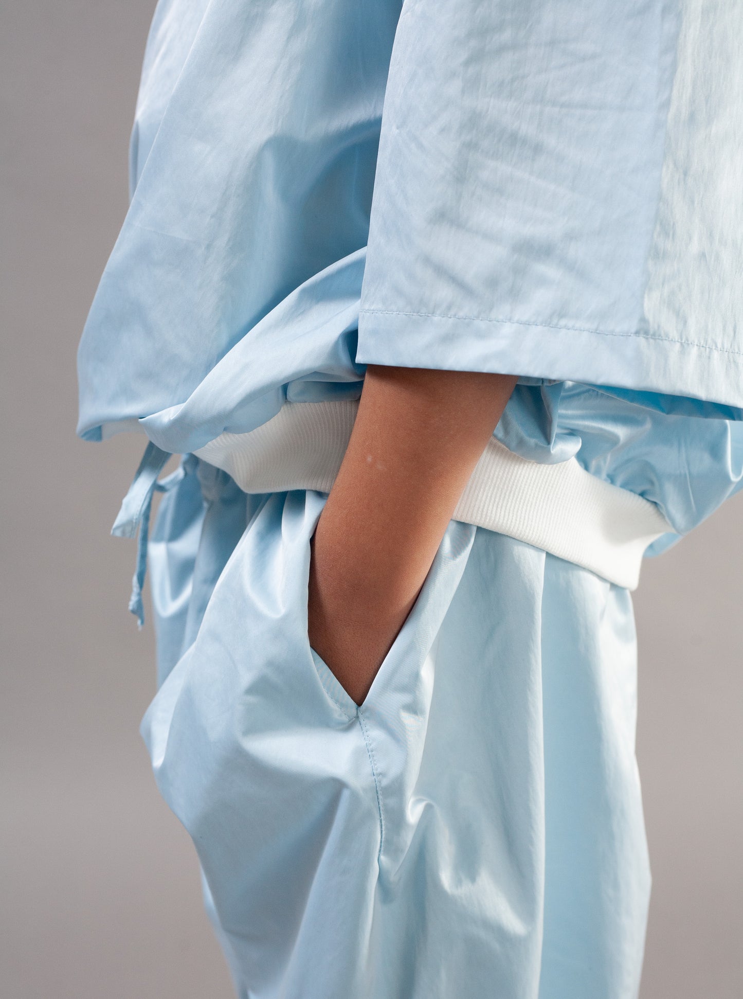 A close-up of a person wearing light blue wide-leg pants with a white elastic waistband and a matching light blue top, with one hand in a pocket.