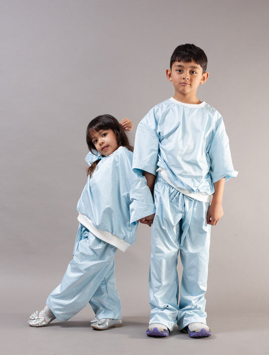 Two children modeling light blue kids sets with white ribbing, standing against a plain gray studio background.