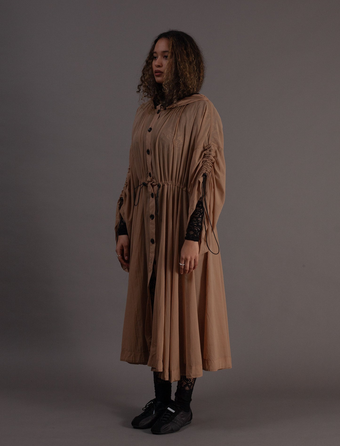 Woman wearing a long beige coat against a grey background
