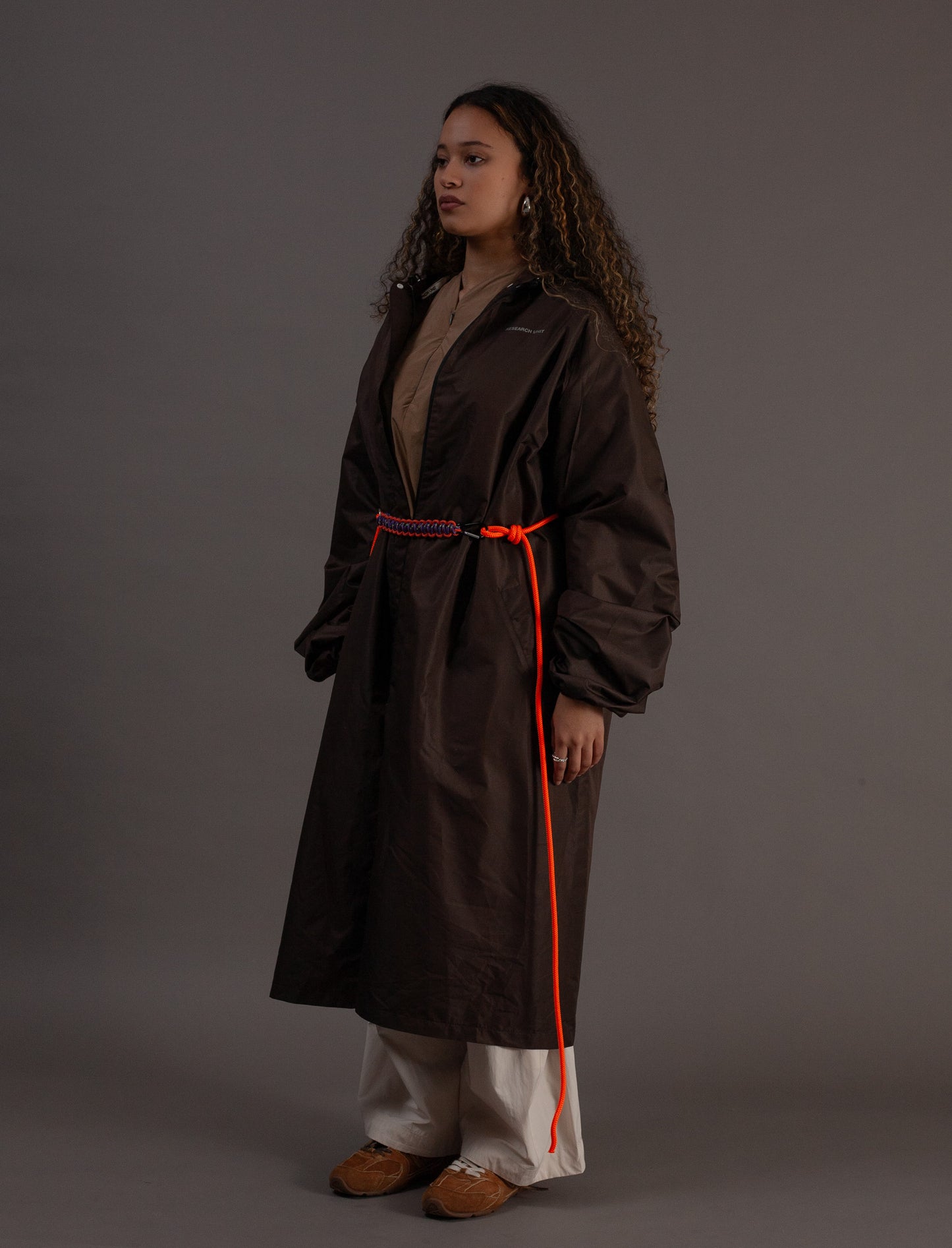 Woman wearing a brown coat with a orange rope on a grey background