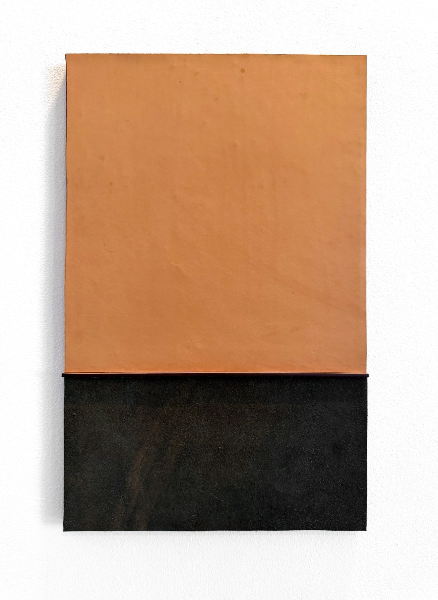 A minimalist abstract wall art piece featuring a large warm tan-orange rectangle on the upper half and a textured black rectangle on the lower half, mounted against a plain white wall.