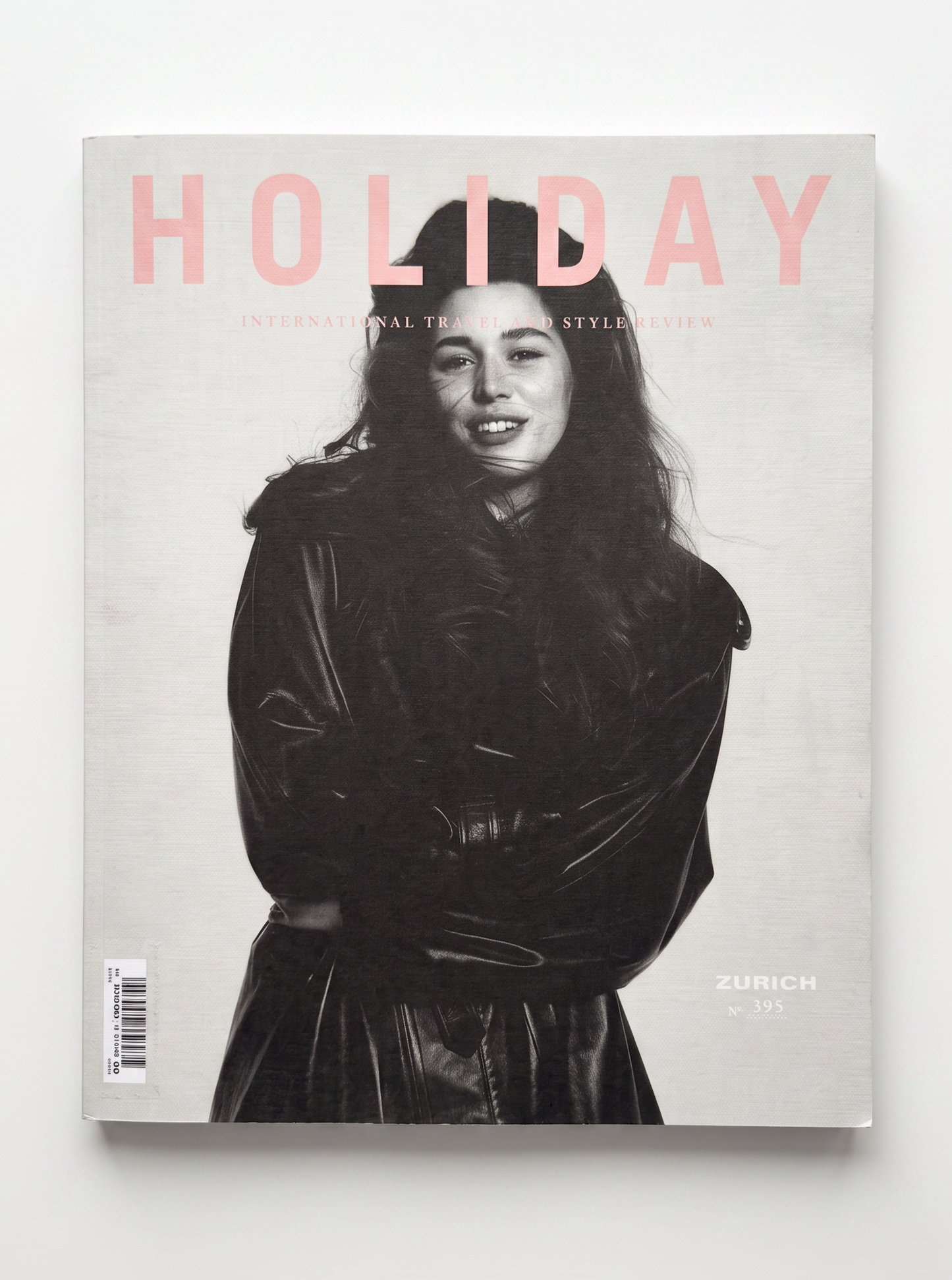 A magazine titled 'HOLIDAY' with a black-and-white portrait cover of a woman in a dark coat, photographed against a light gray background.