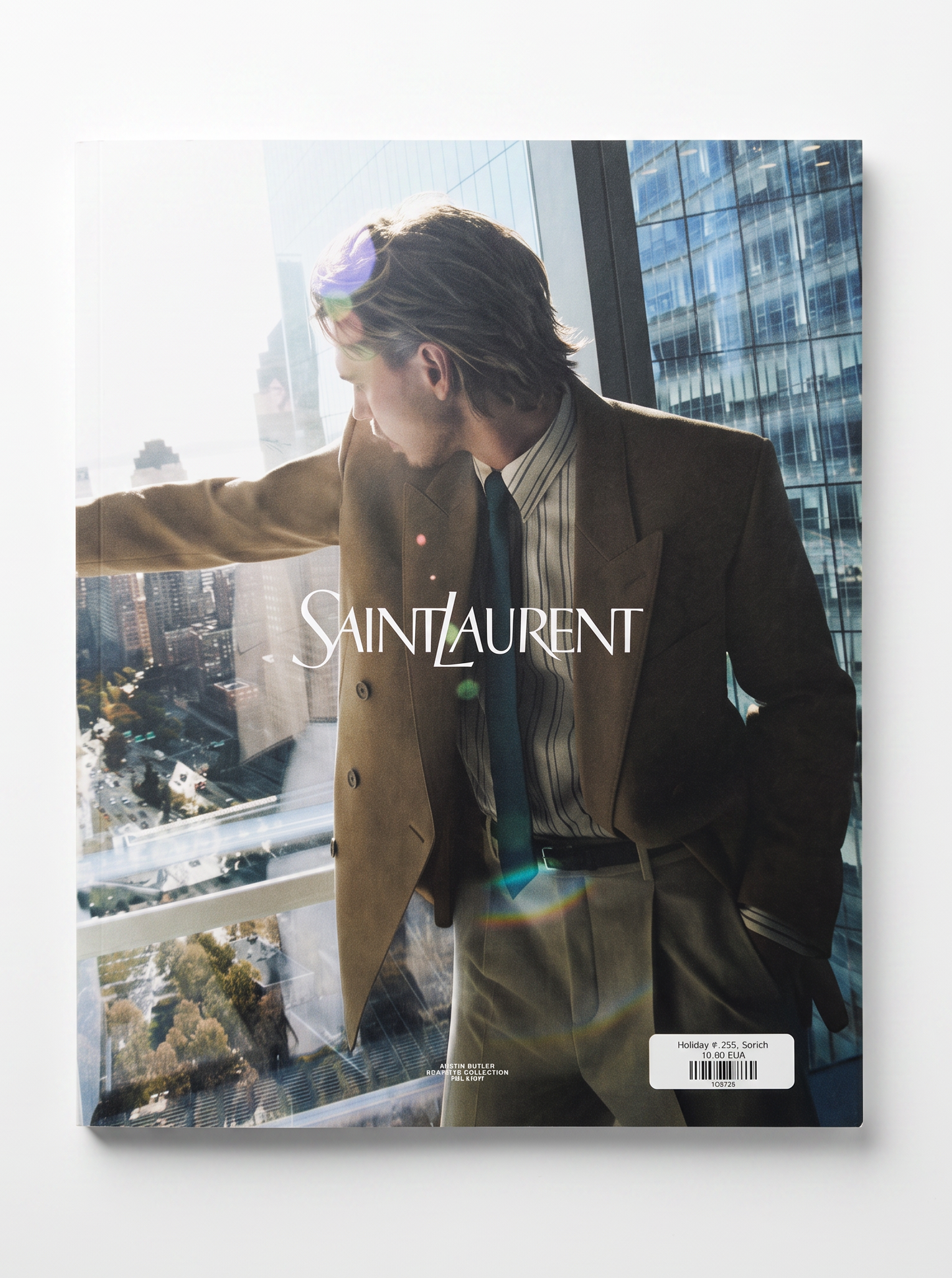 A Saint Laurent fashion magazine or book cover featuring a man in a brown suit and striped shirt leaning by a window with a city skyline outside. The title SAINT LAURENT is printed across the center, and a barcode label is visible at the bottom right.
