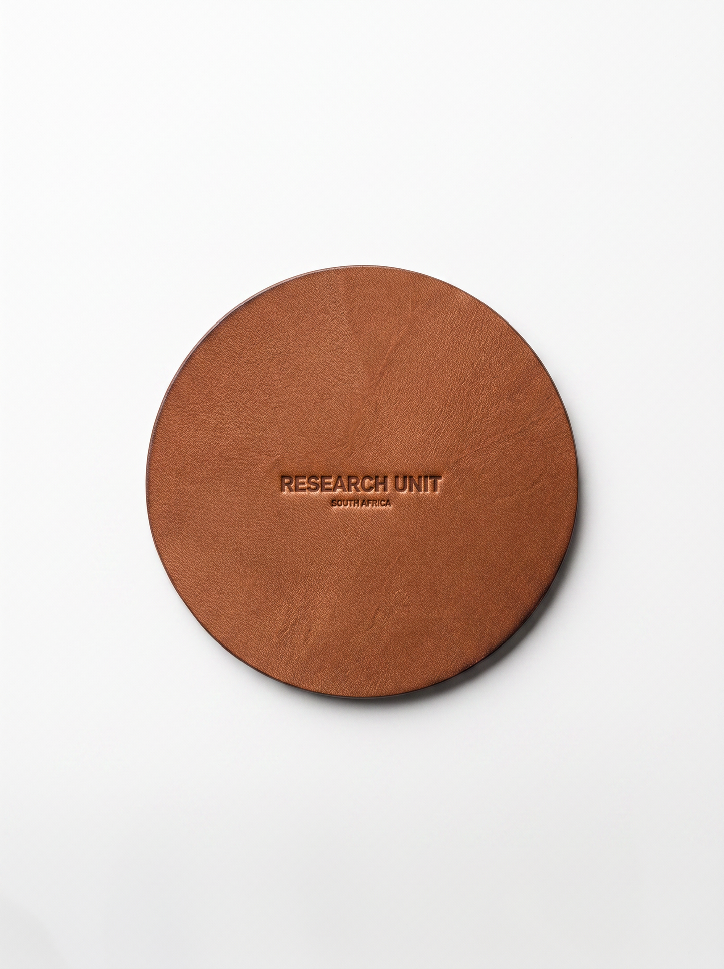 A round brown leather coaster with 'RESEARCH UNIT' embossed in the center, photographed from directly above on a clean white background.