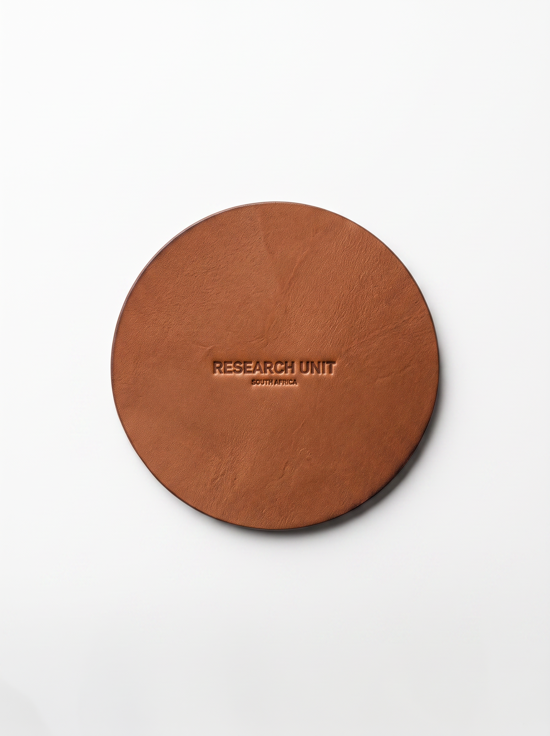 A round brown leather coaster with 'RESEARCH UNIT' embossed in the center, photographed from directly above on a clean white background.