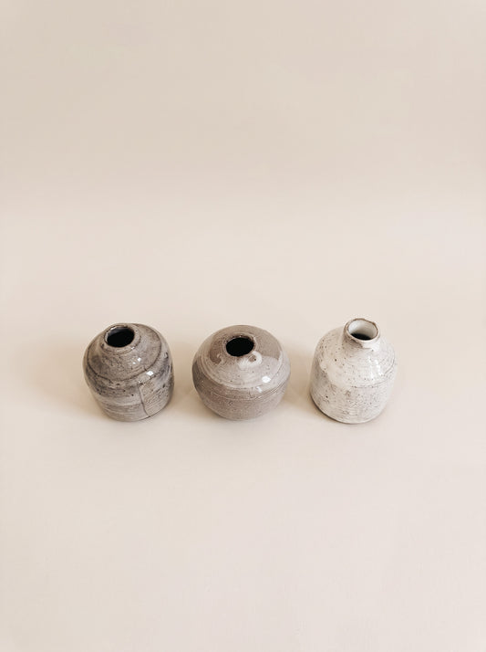 Three small handmade ceramic vases in gray and white glazes, arranged in a row against a solid beige background.