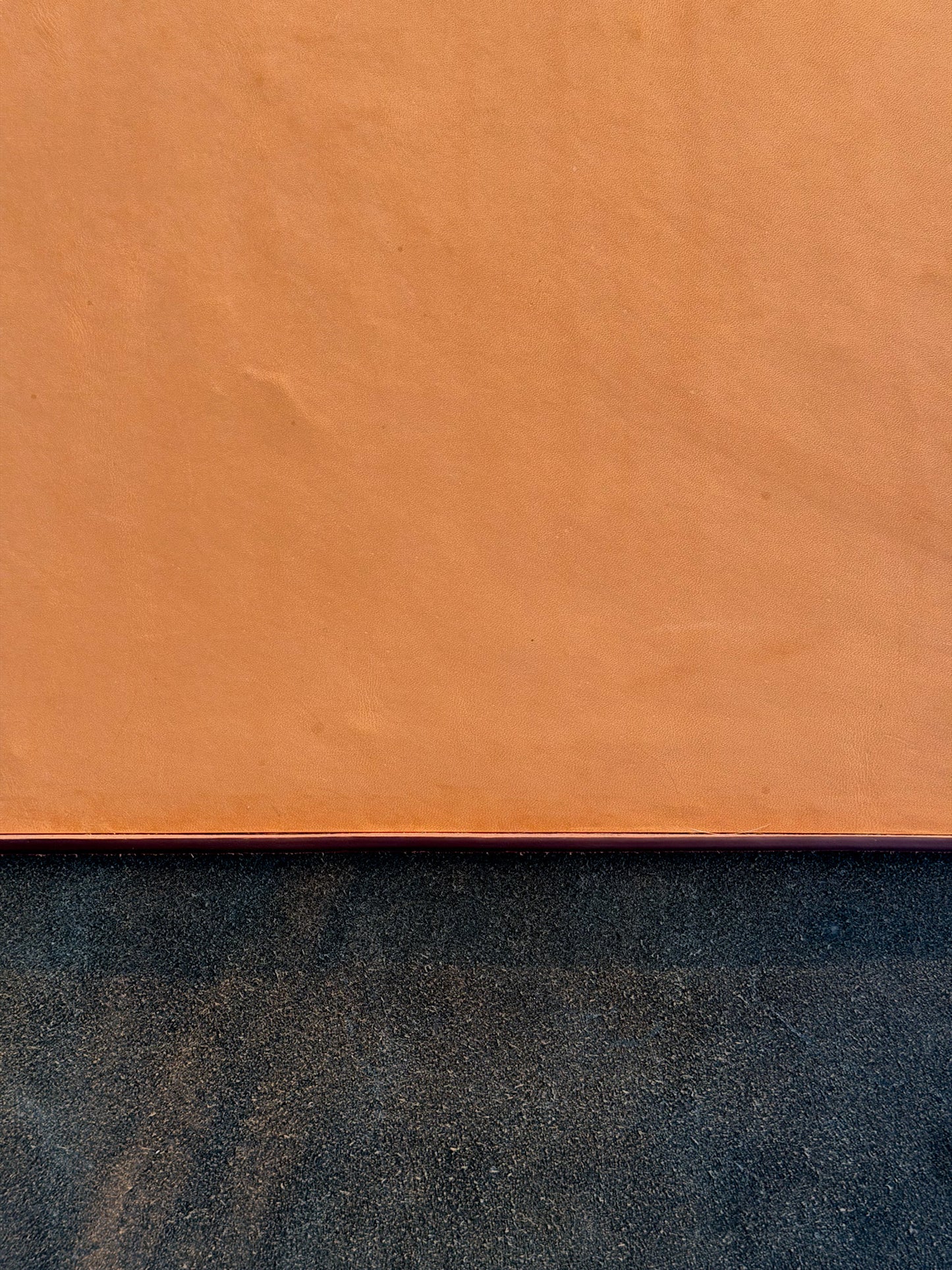 A close-up of a textured orange-brown surface, likely leather or suede, with a dark charcoal textured surface visible along the bottom edge.