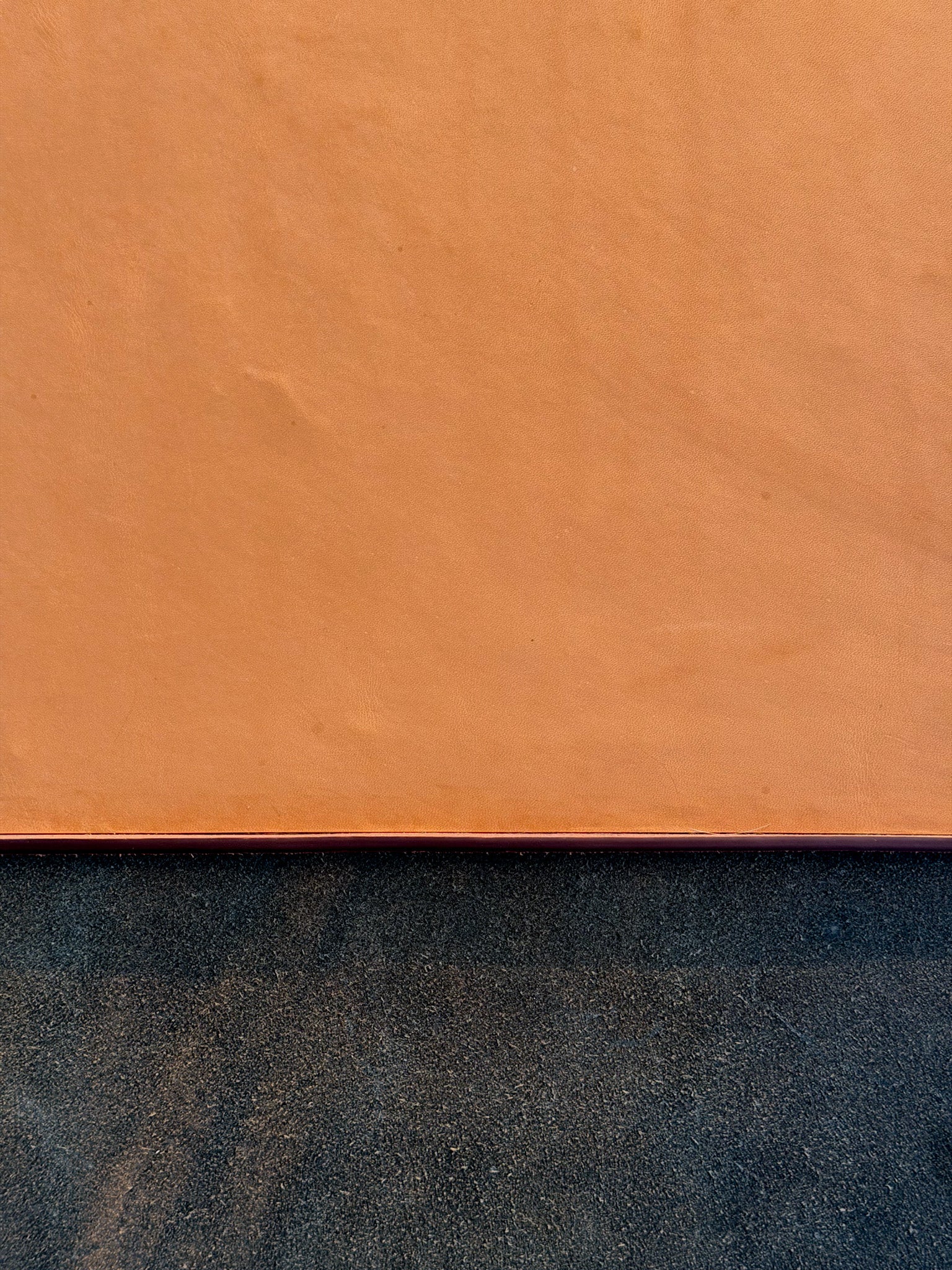 A close-up of a textured orange-brown surface, likely leather or suede, with a dark charcoal textured surface visible along the bottom edge.