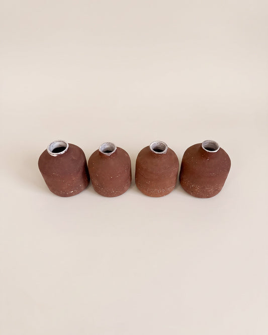 Four small terracotta-colored ceramic vases with a textured matte finish, arranged in a row on a warm beige background.