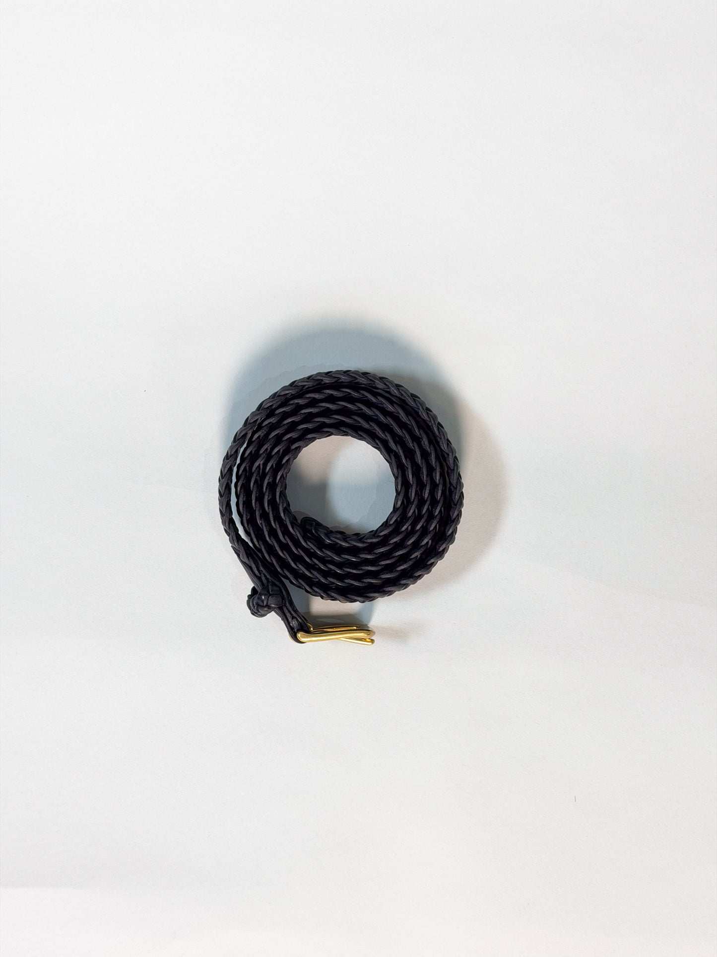 A coiled black braided cord with a small gold metal connector, photographed on a plain white background.
