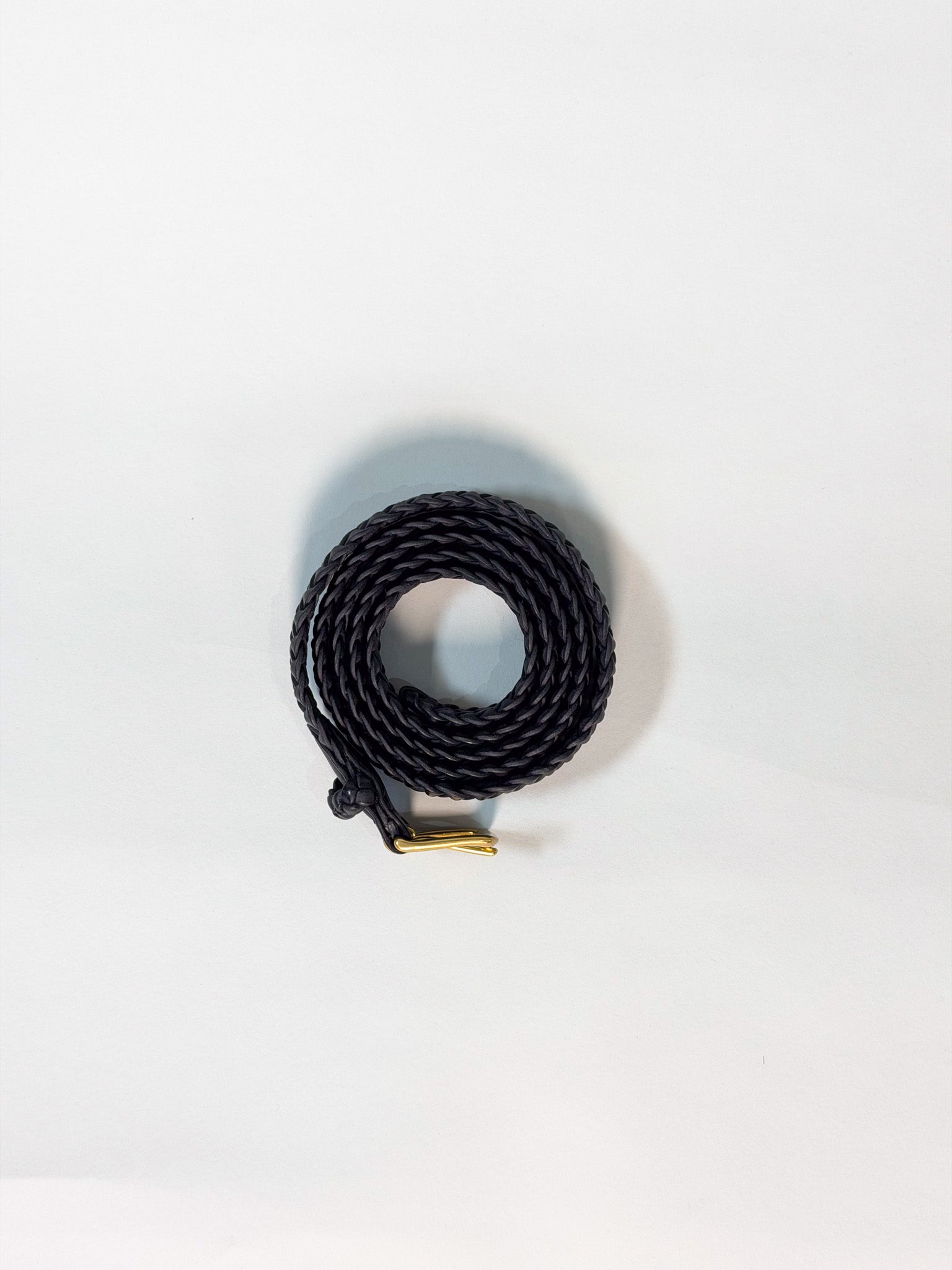 A coiled black braided cord with a small gold metal connector, photographed on a plain white background.