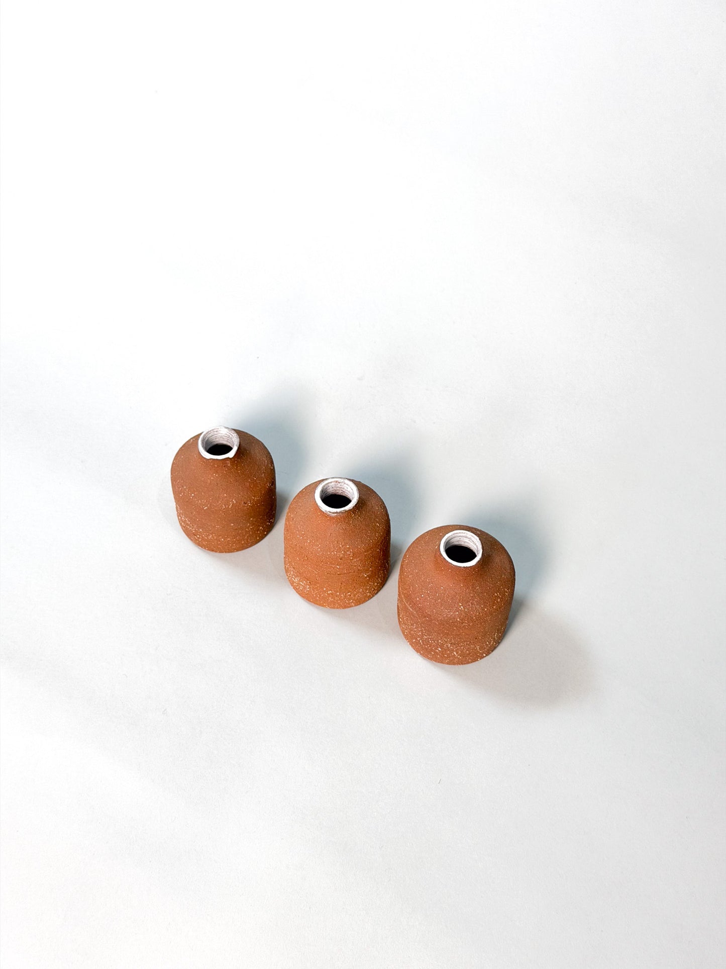 Three small terracotta-colored ceramic vases arranged diagonally on a clean white background.