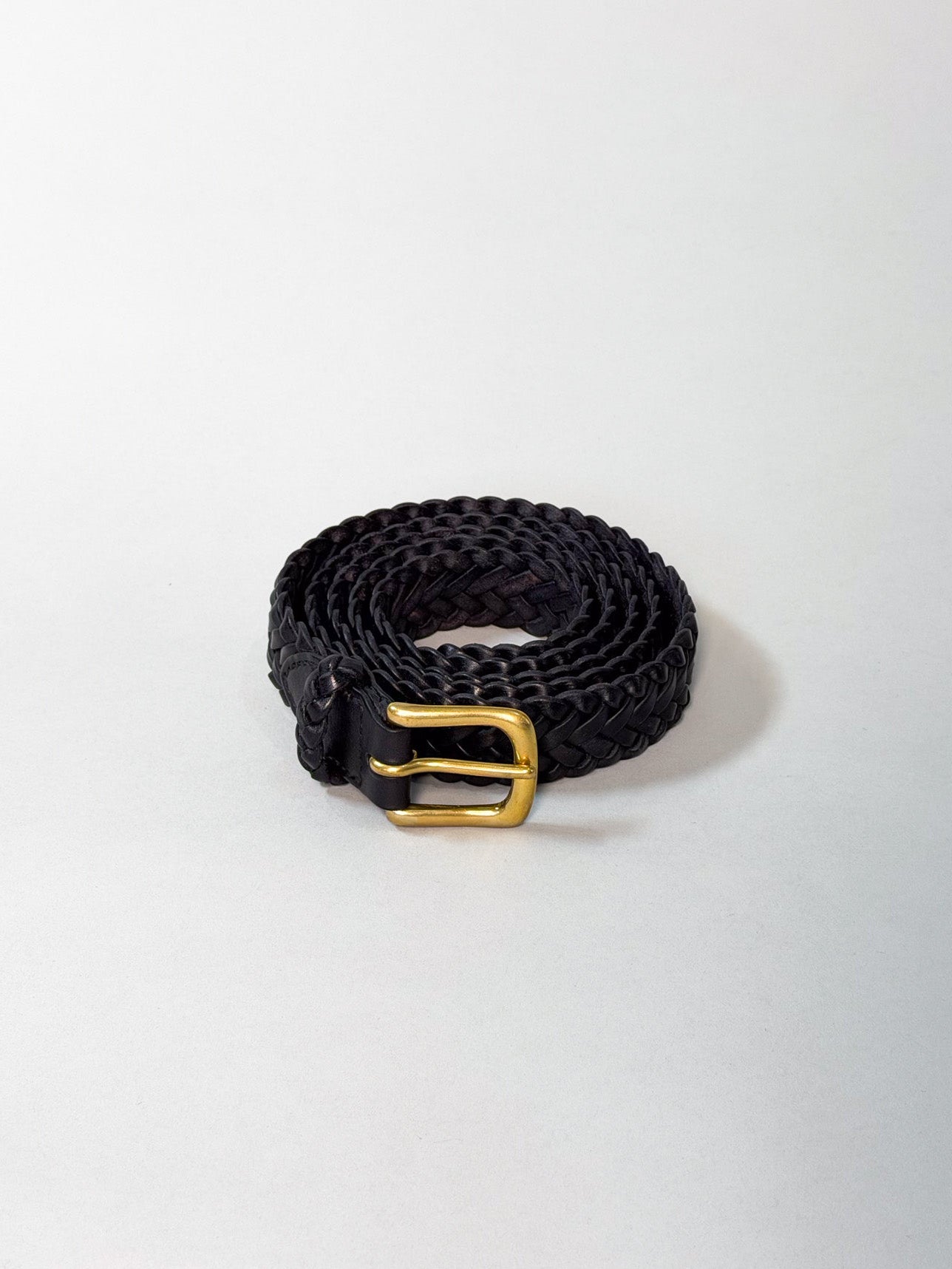 A black braided leather belt with a polished gold buckle, coiled on a light gray background.