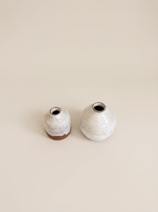 Two small ceramic vases with a speckled white and gray glaze and a natural brown clay base, displayed on a solid beige background.