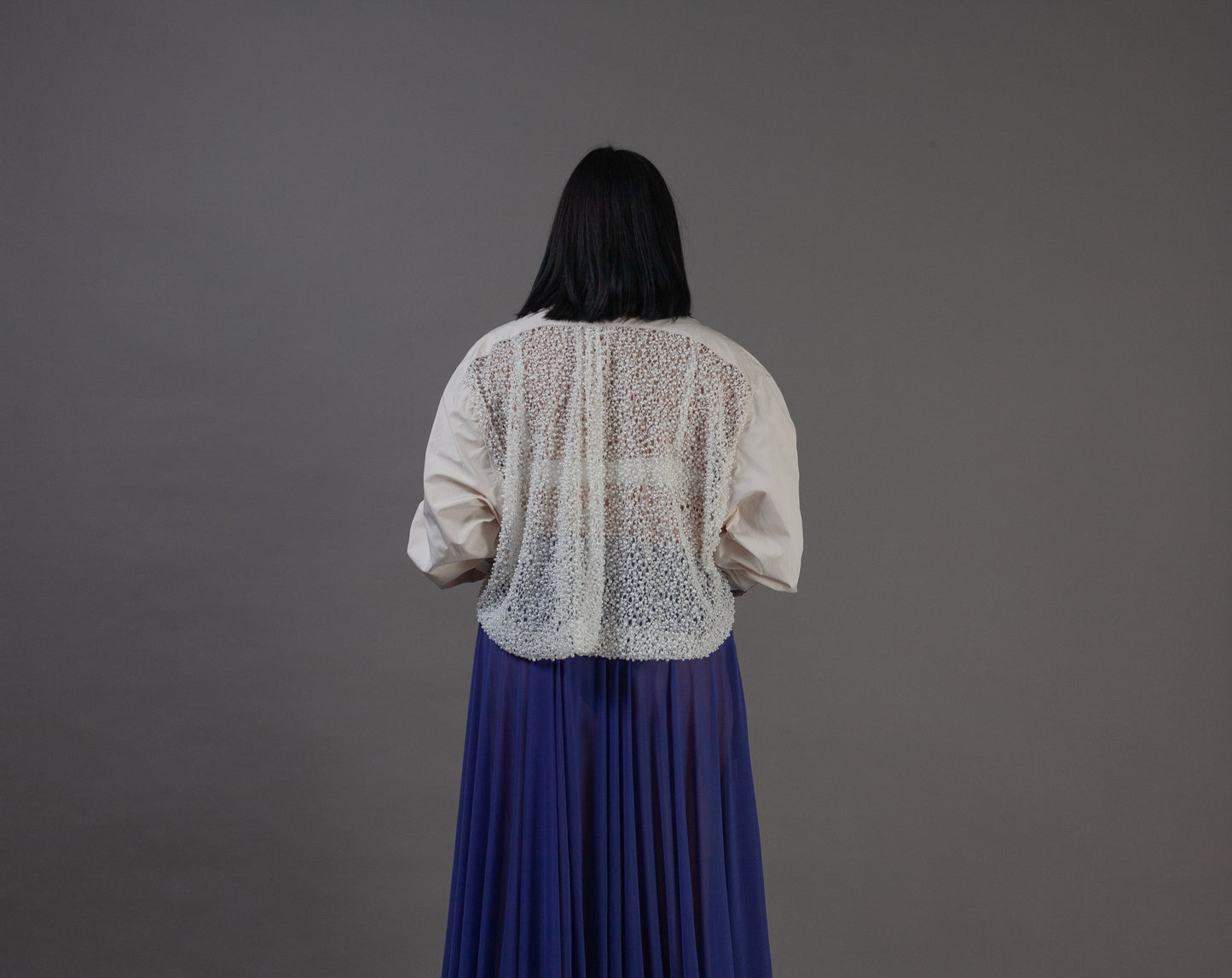 Person wearing a white blouse with pearl back details 