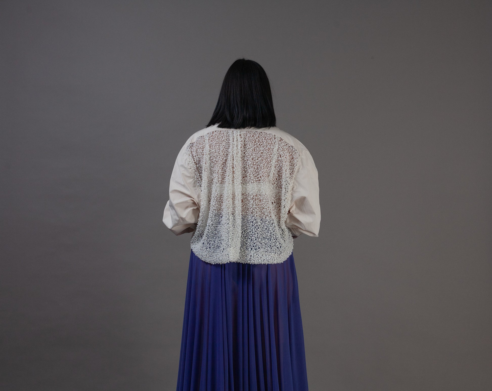 Person wearing a white blouse with pearl back details 