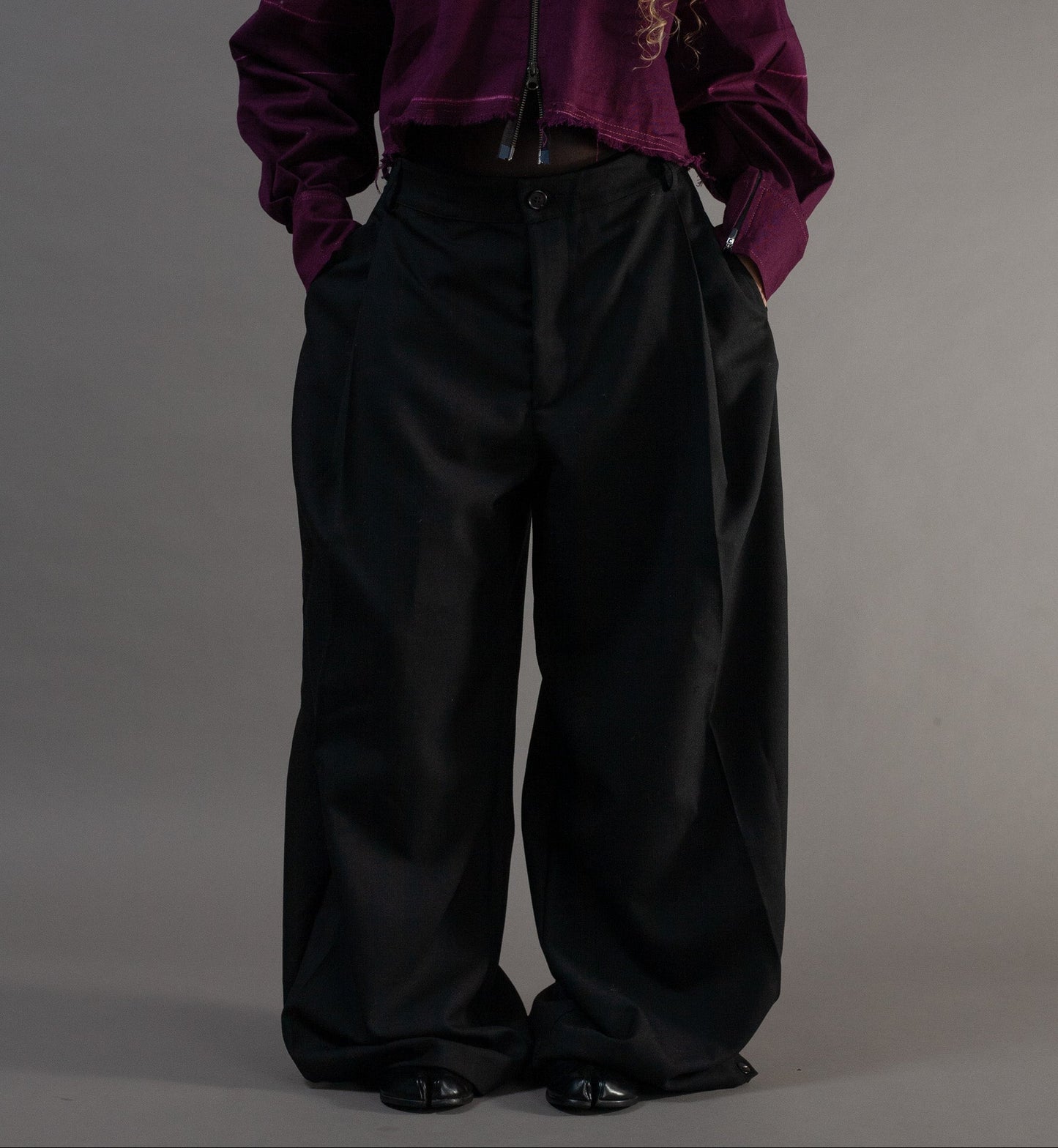 Person wearing a purple jacket and black pants on a grey background